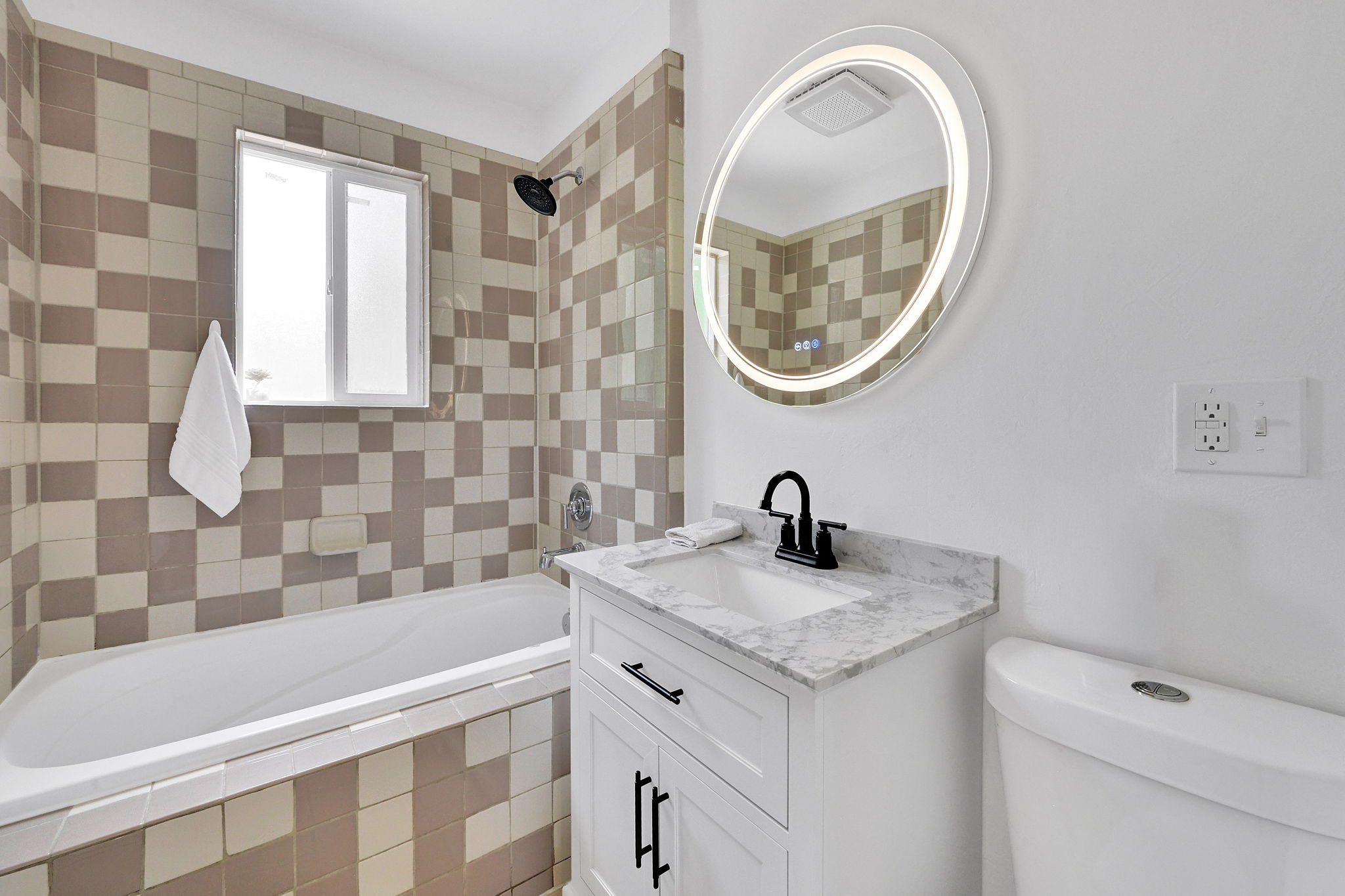 Bathroom featuring a white vanity with a stone countertop, an illuminated oval mirror, a white bathtub, and a tiled shower surround with a checkerboard pattern