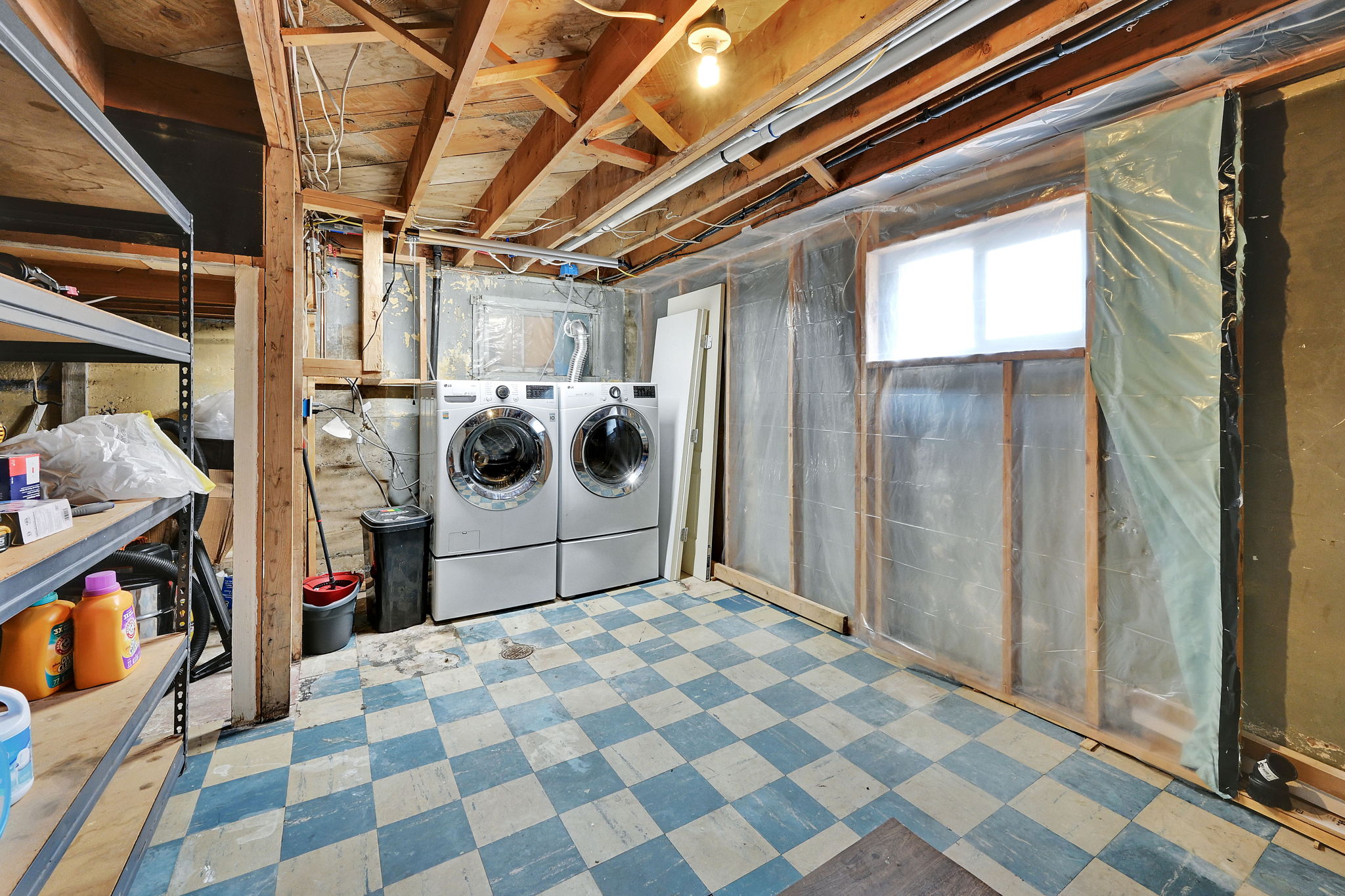 Utility area featuring wood ceiling beams, exposed pipes, a double window, checkerboard flooring, and a washer and dryer set