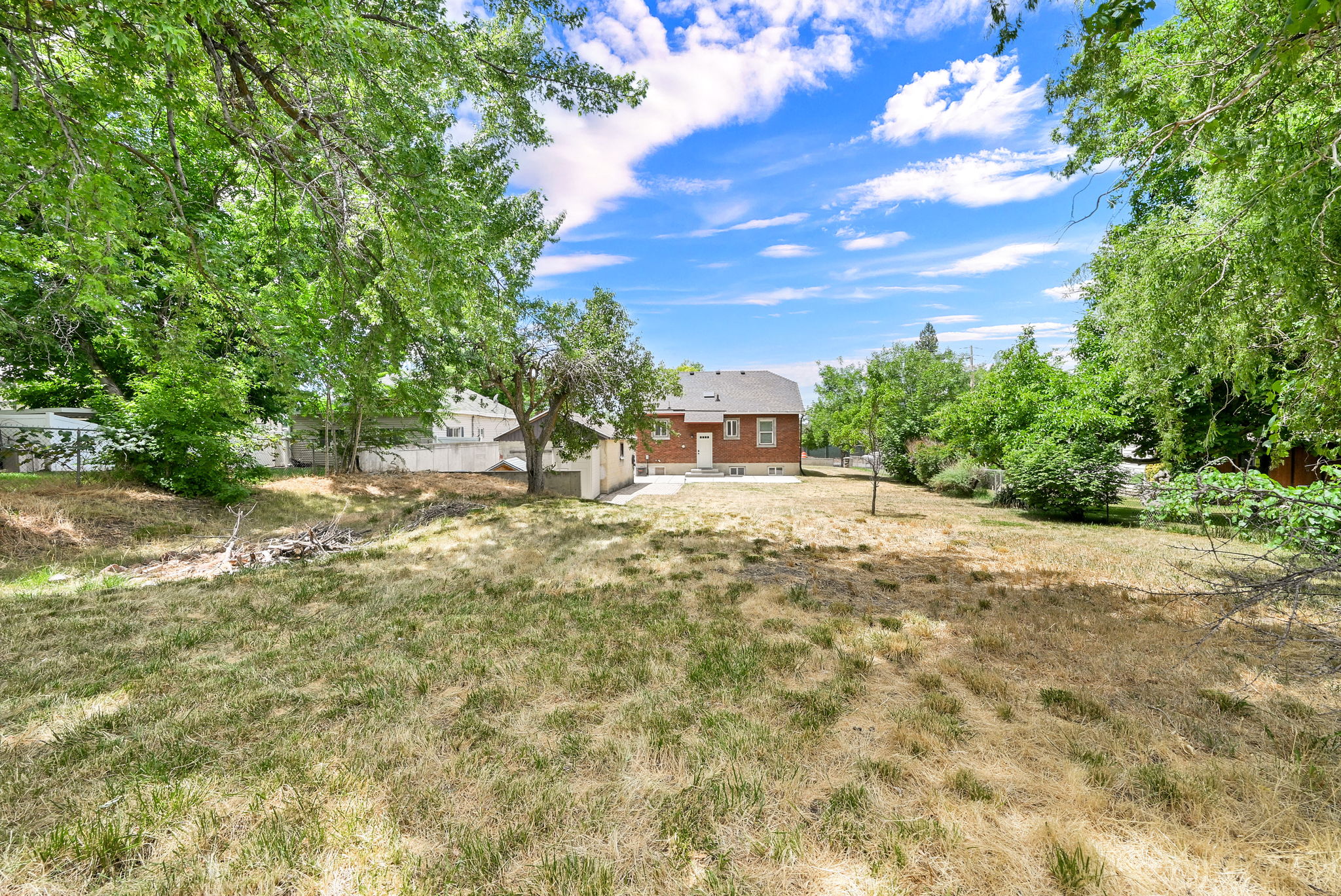 Expansive property featuring a red brick house with white trim, a detached white garage structure, and mature trees providing natural shading