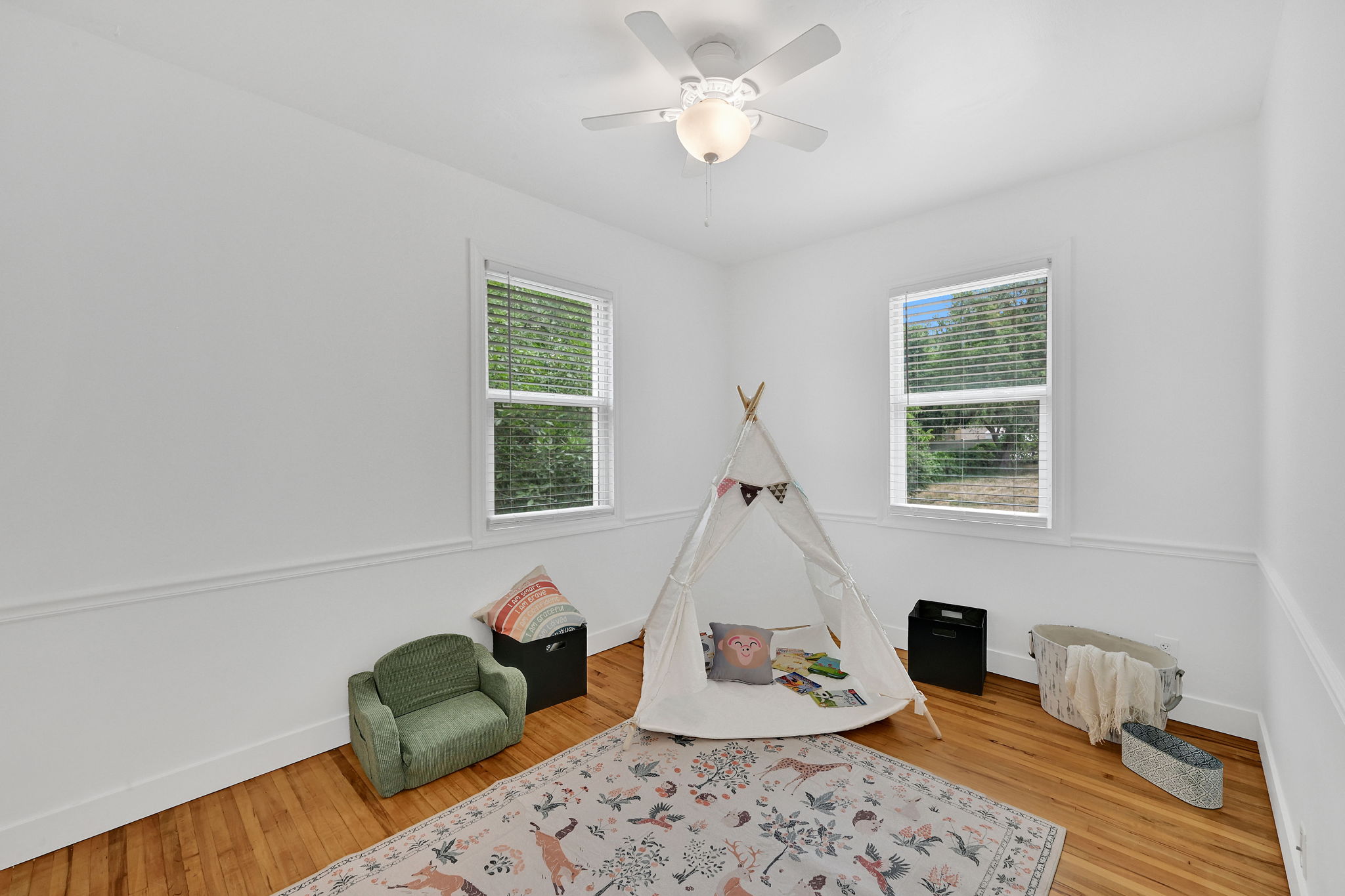Bright room featuring two windows with horizontal blinds, hardwood flooring, white baseboards, and a ceiling fan with integrated lighting