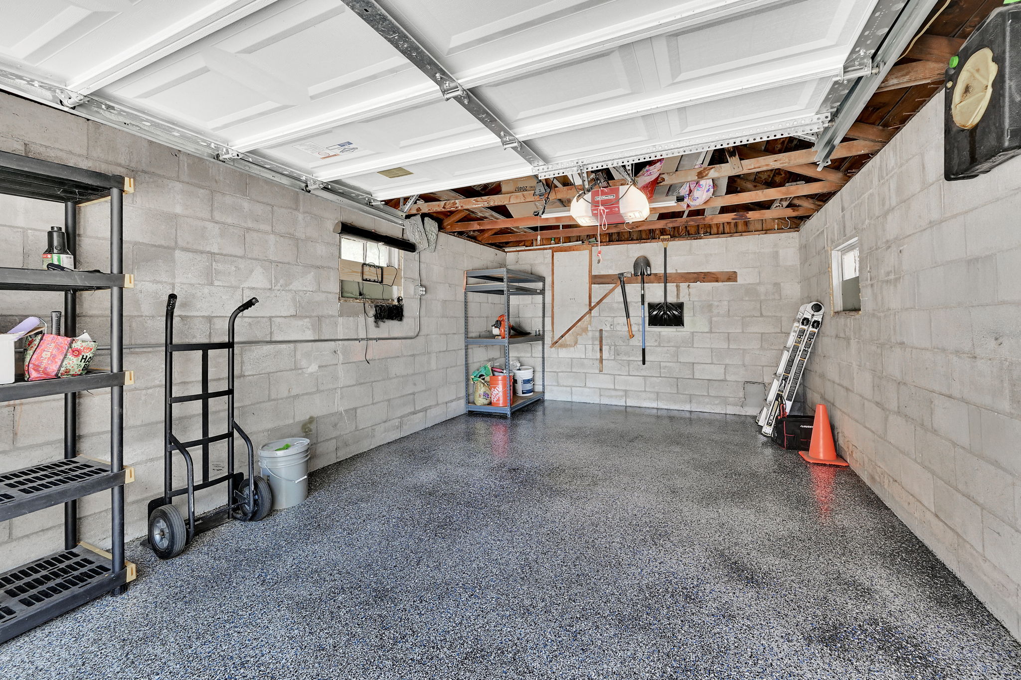 Spacious garage featuring a durable speckled epoxy floor, concrete block walls, exposed wood beam ceiling, and a white paneled garage door