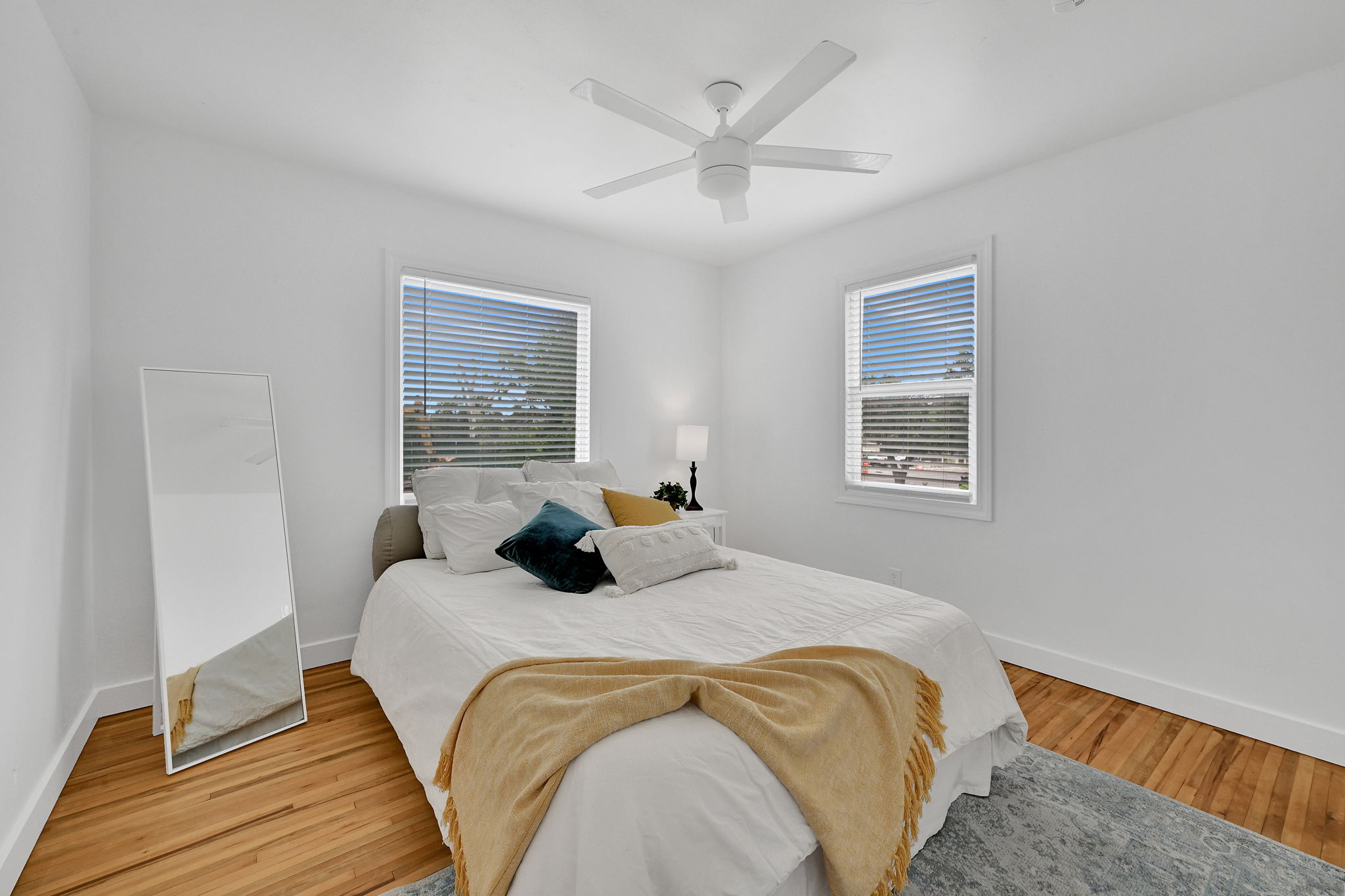Bedroom featuring wood-finish flooring, two windows with blinds, a white ceiling fan, and white walls with baseboards