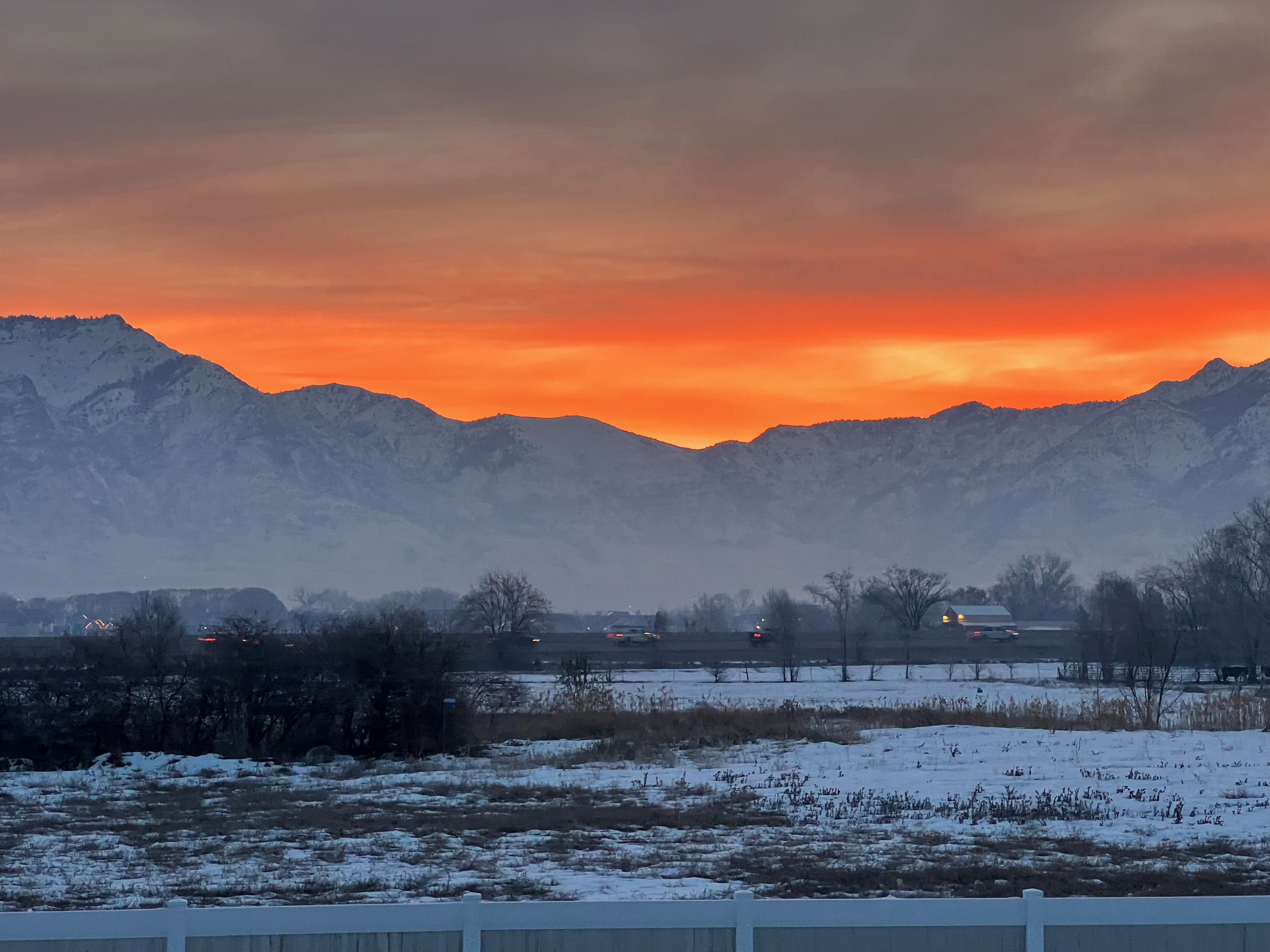 Sweeping mountain range backdrop with a dramatic sunset, featuring a snow-dusted foreground and a white vinyl fence