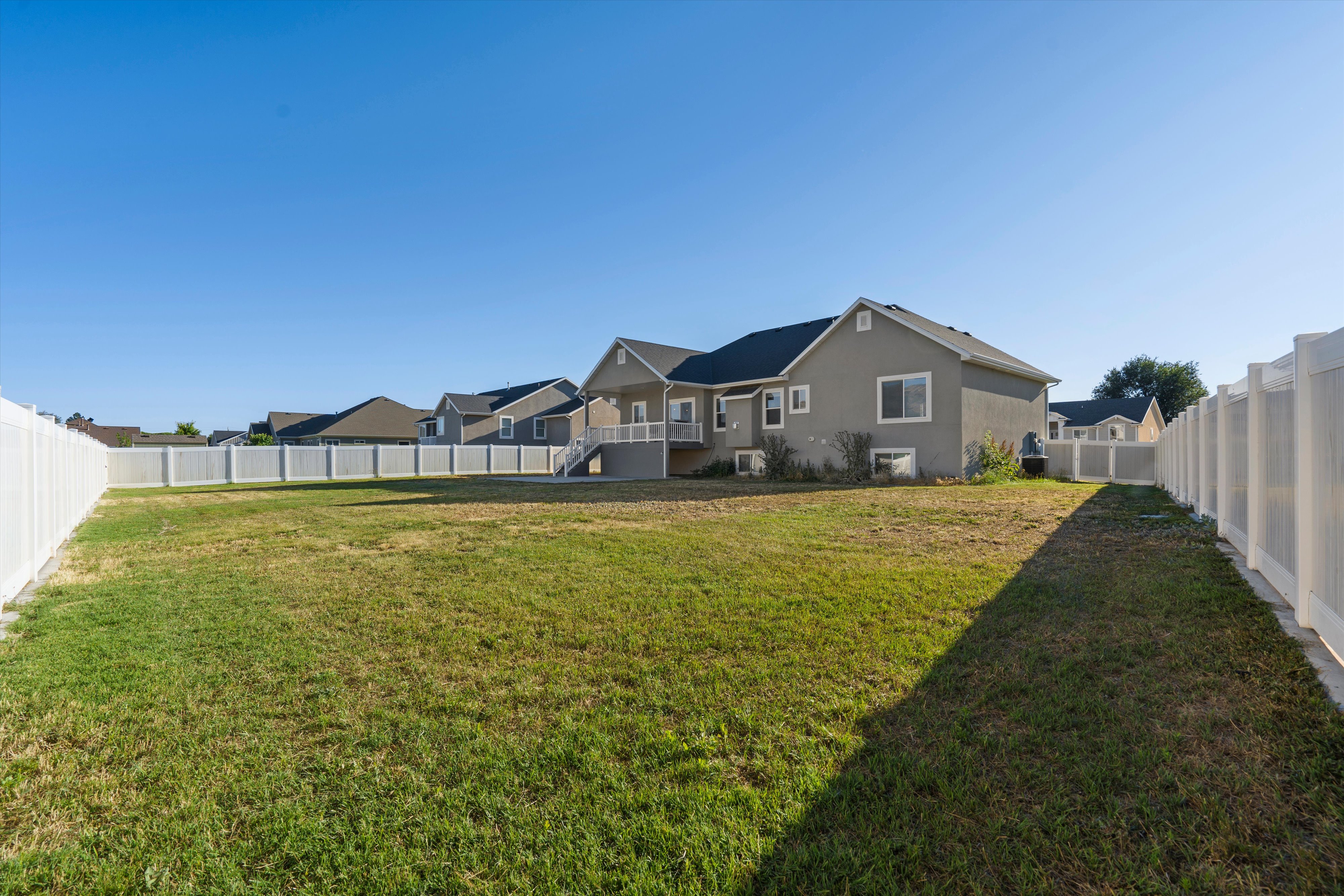 Expansive backyard featuring a large grass area, full vinyl fencing, and a two-story residence with a rear deck