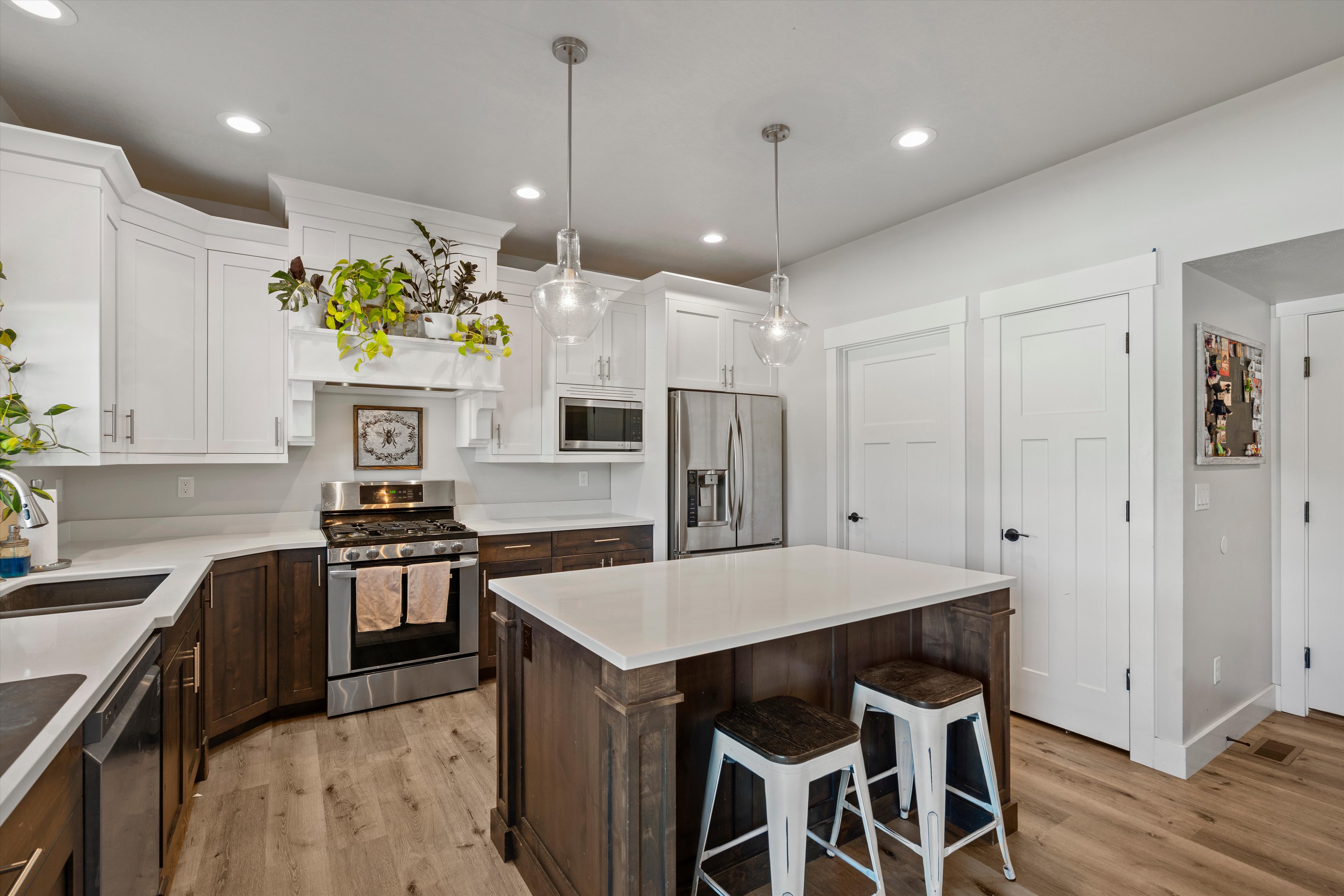 Kitchen featuring a wood-finish flooring, white upper cabinetry, dark wood-finish lower cabinetry, a center island with pendant lighting, and stainless steel appliances