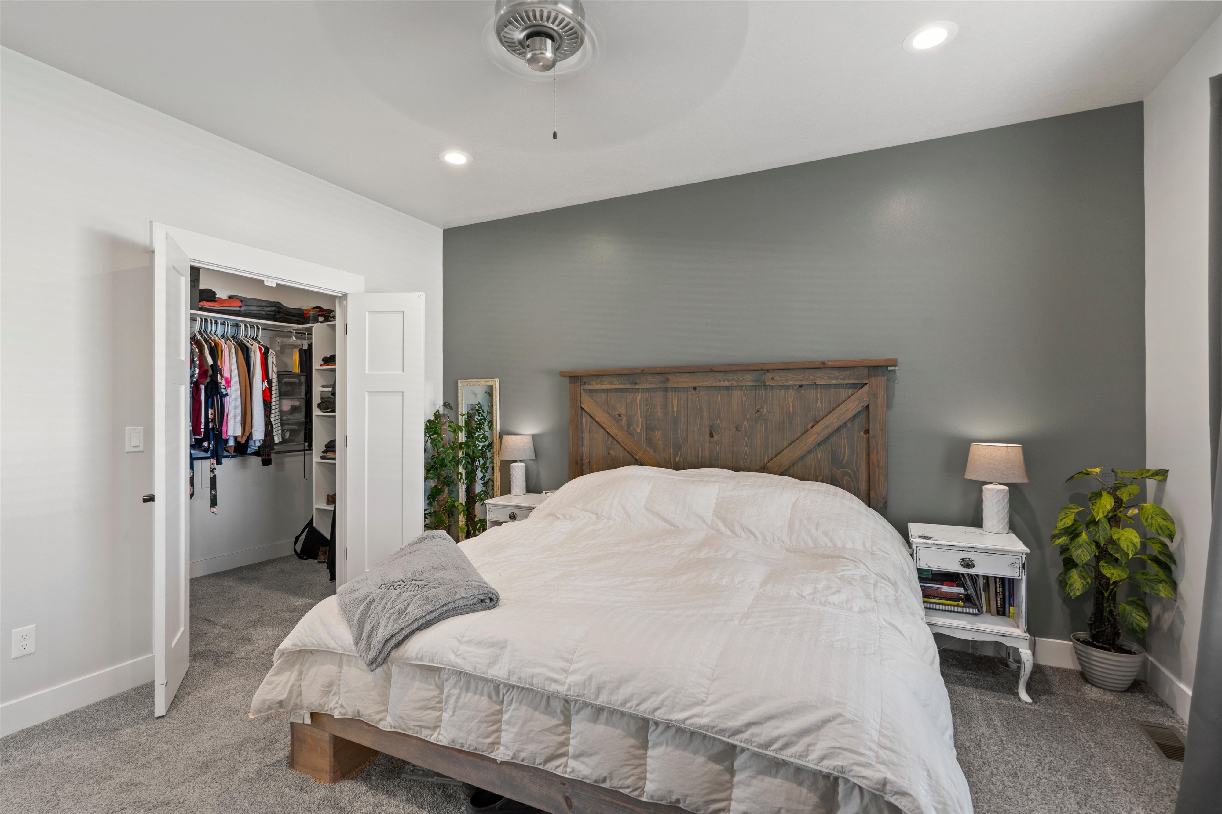 Spacious bedroom featuring light gray carpet flooring, a dark gray accent wall, and recessed lighting