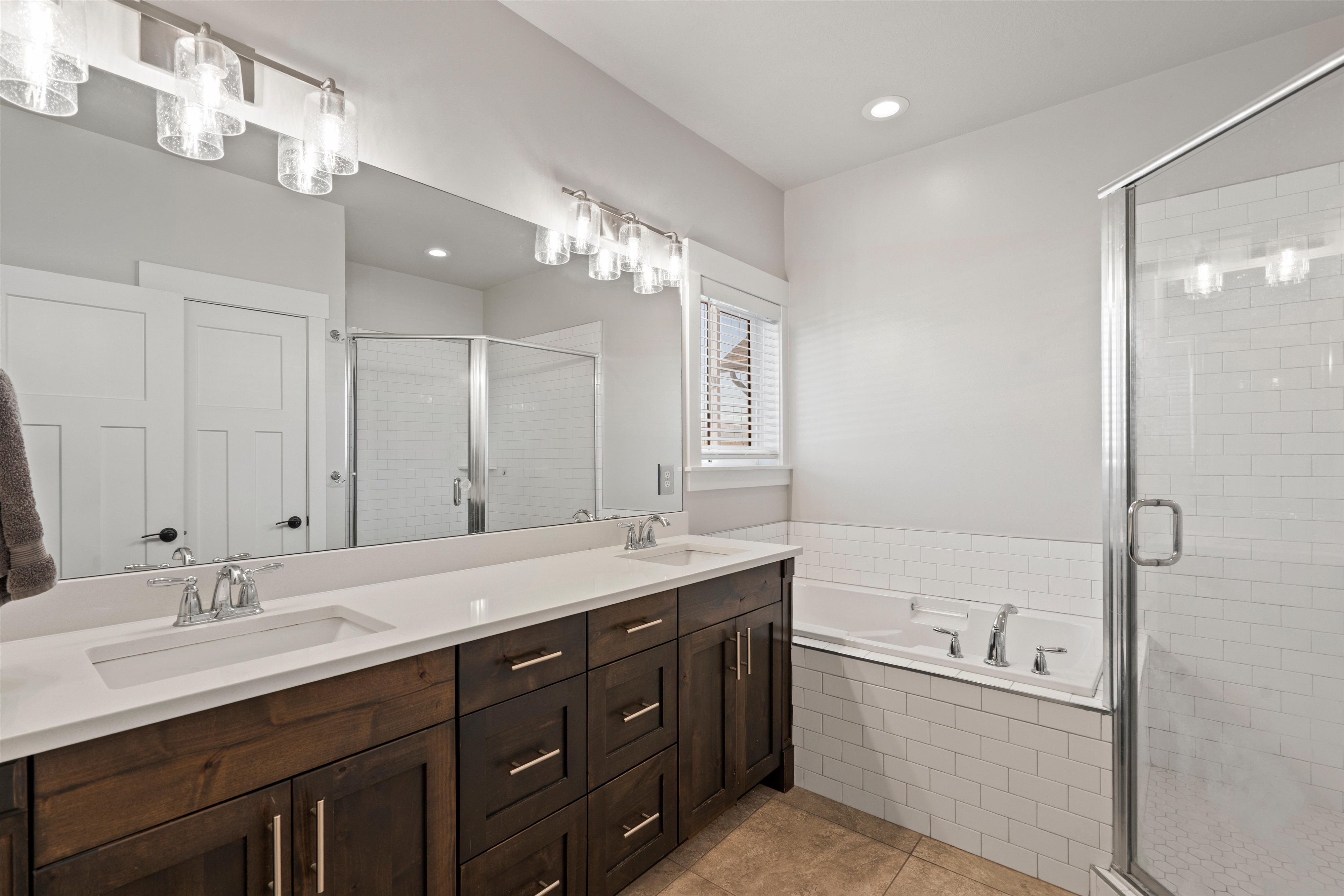 Bathroom featuring a double vanity with dark wood cabinetry and white countertops, a large framed mirror, and chrome fixtures