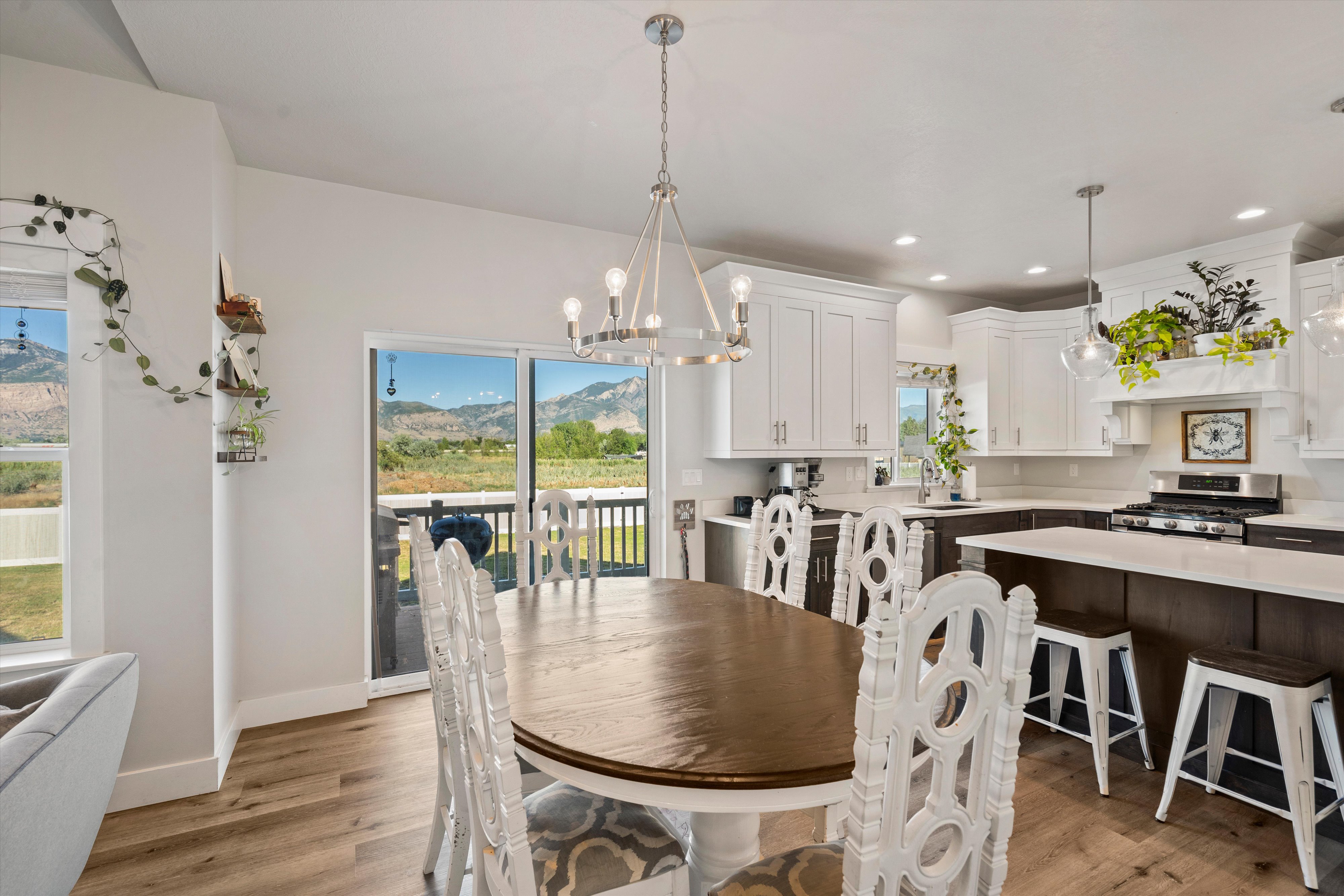 Open-concept living space featuring wood-finish flooring, a contemporary dining chandelier, recessed lighting, white upper cabinetry, and a kitchen island with seating
