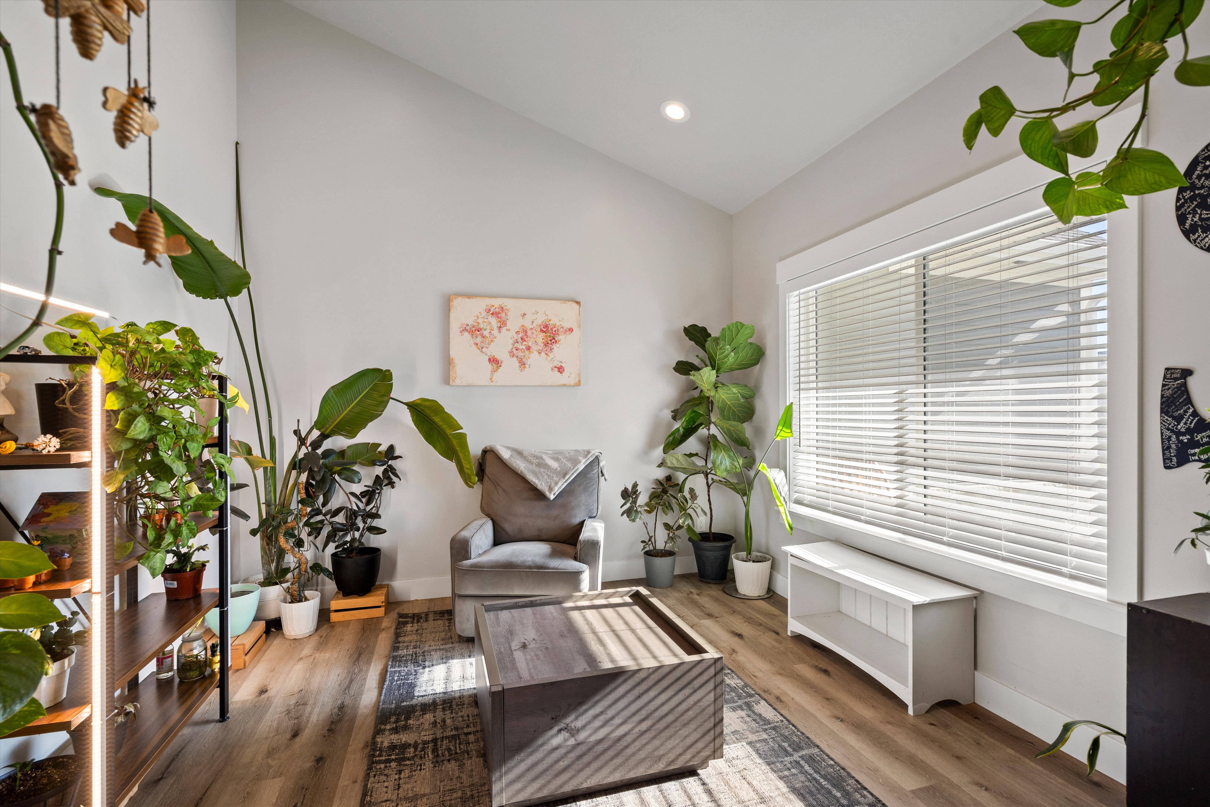 Vaulted ceiling living area featuring wood-finish flooring and ample natural light from a large window with blinds
