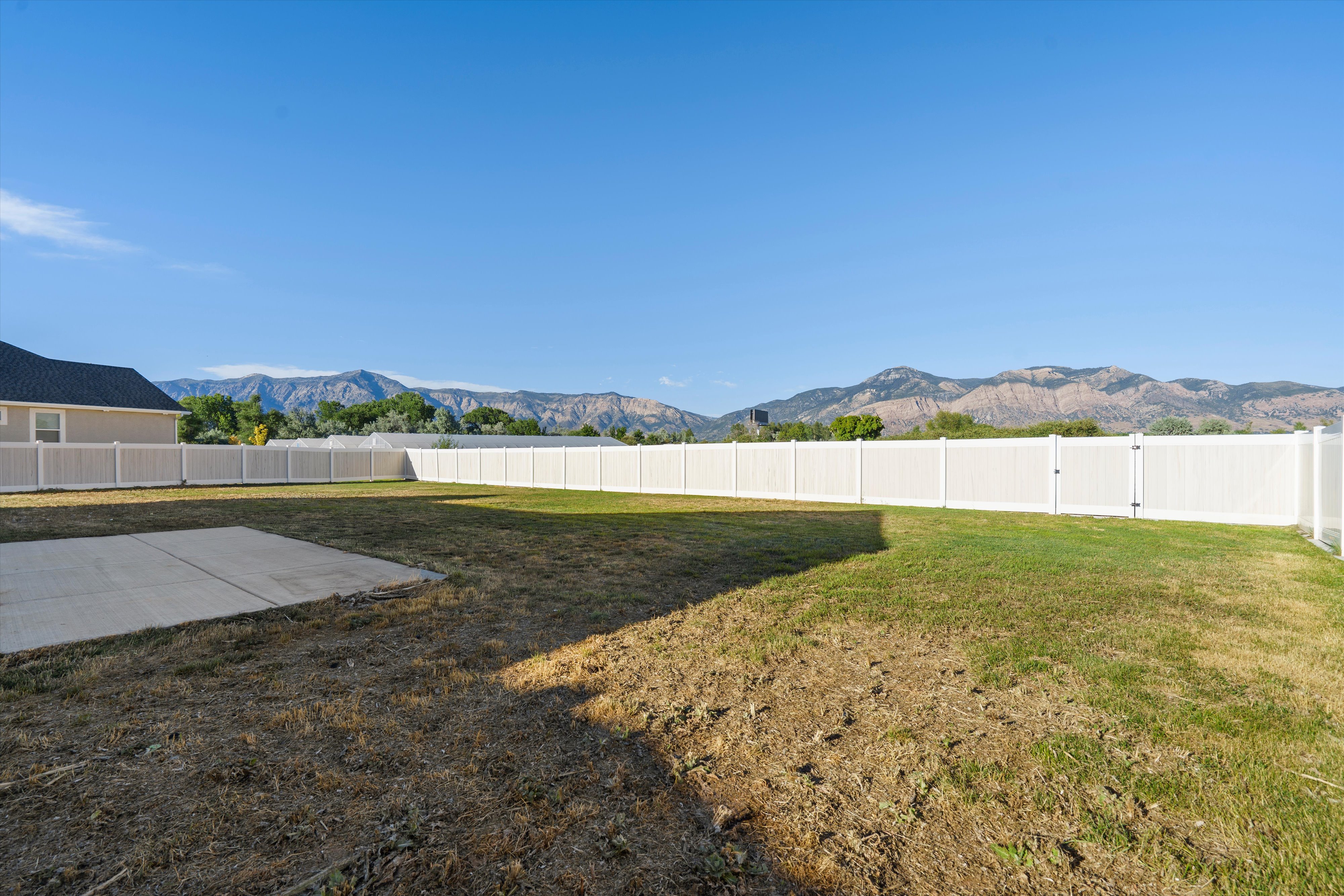 Expansive rear yard featuring a concrete patio pad, white privacy fencing, and distant mountain scenery