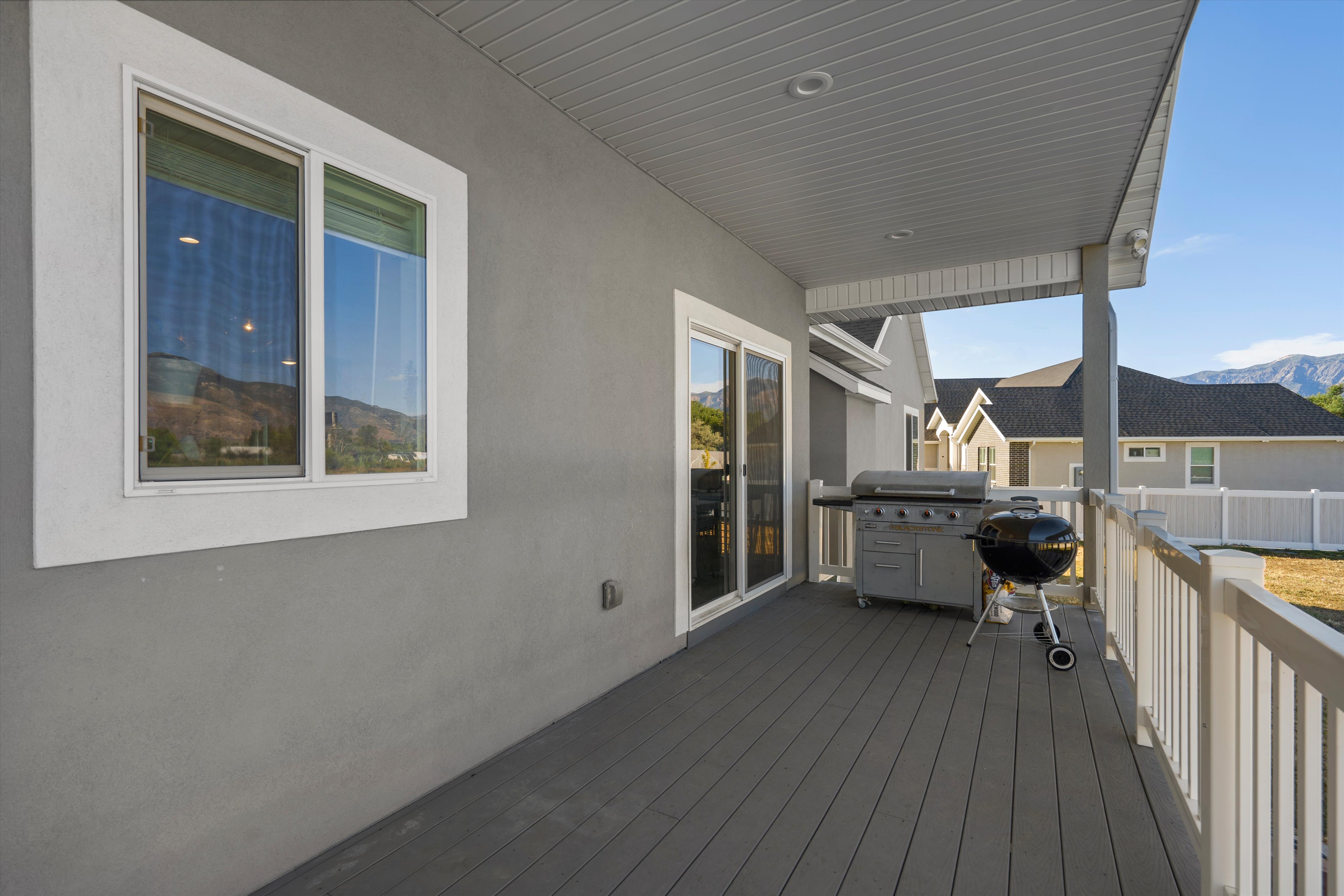 Covered back deck featuring composite decking, stucco exterior, white railing, and sliding glass door access