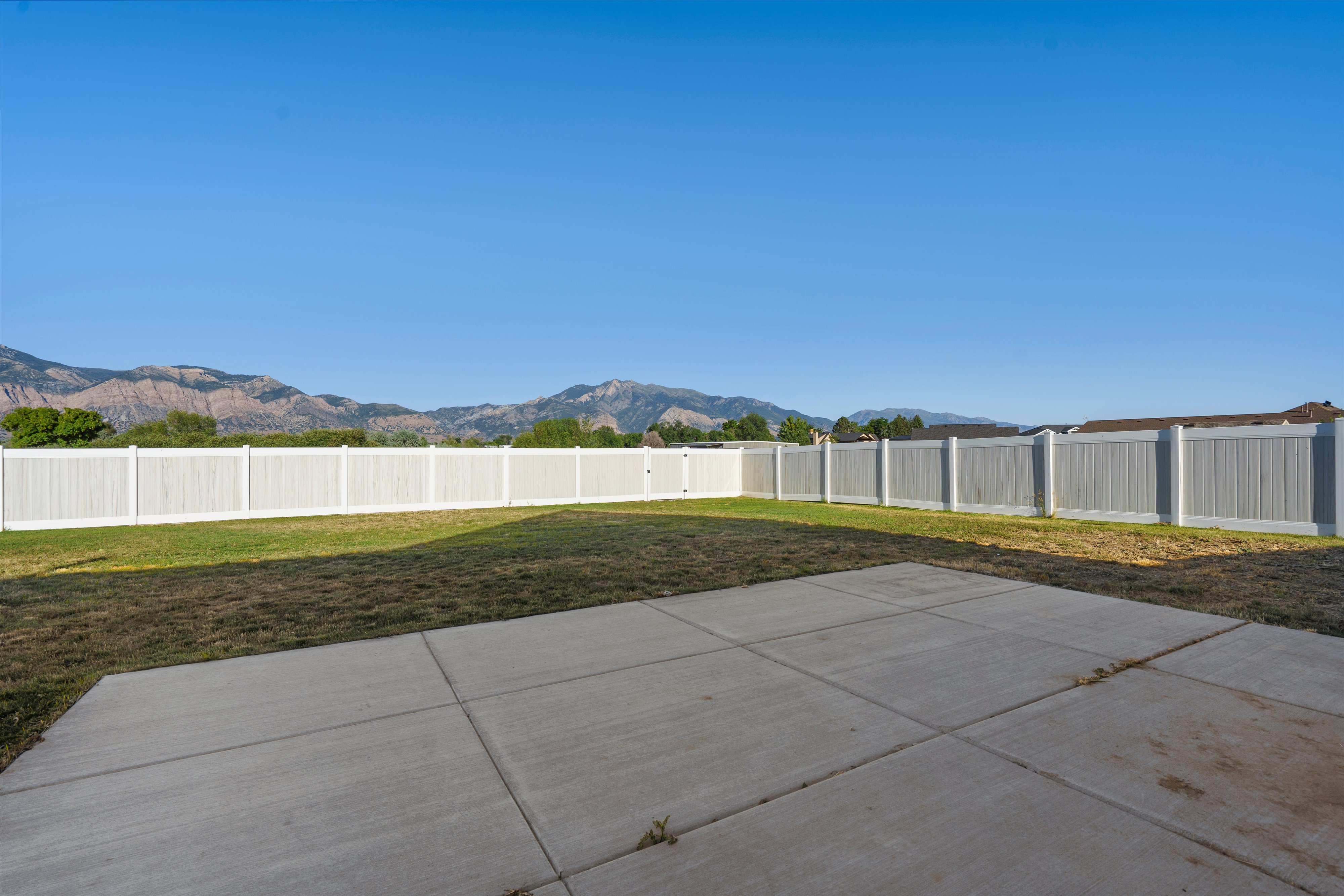 Expansive backyard featuring a concrete patio, a partial lawn, and a white perimeter fence