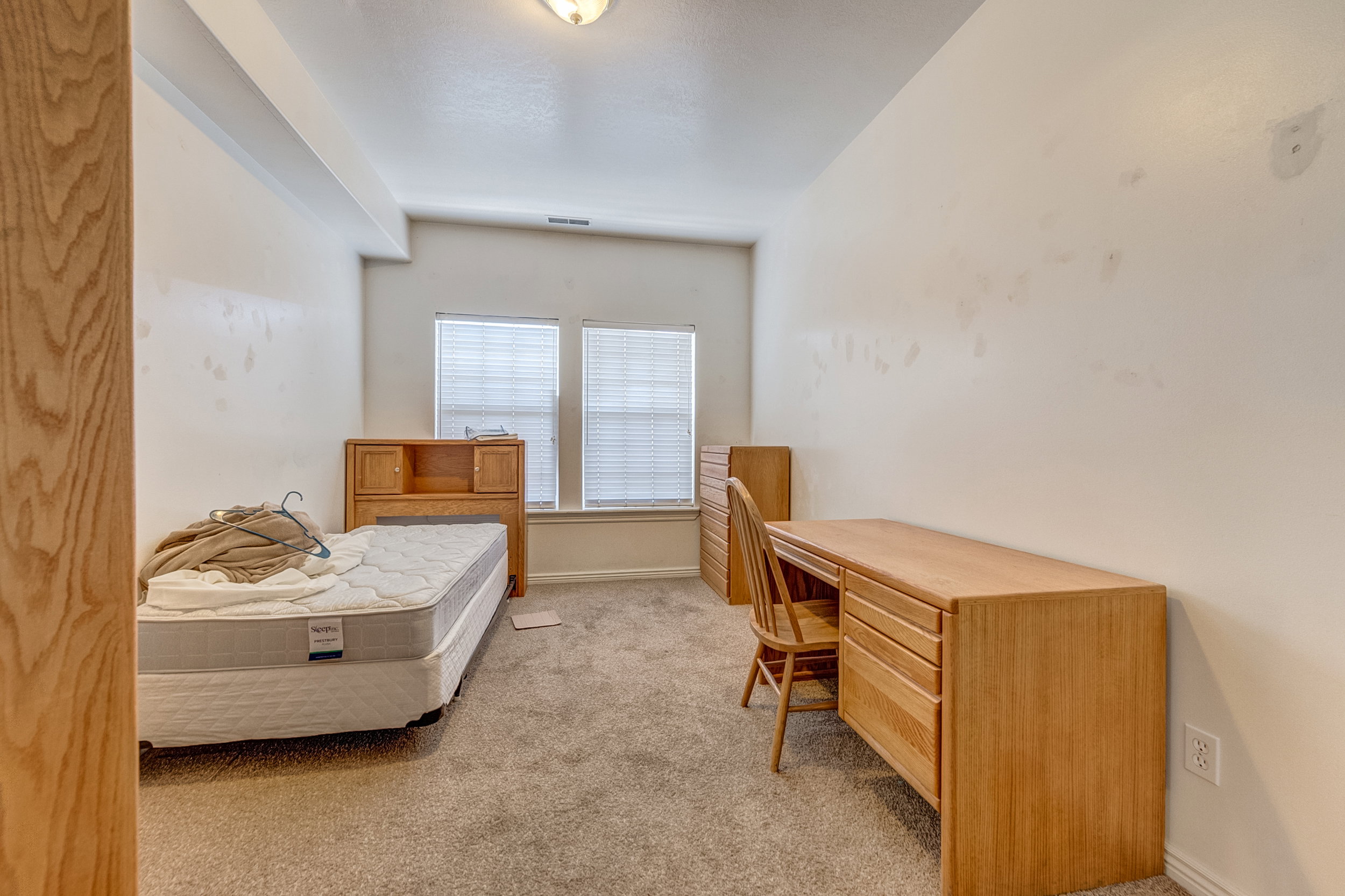 Carpeted room featuring dual windows with blinds, a ceiling-mounted light fixture, and a built-in architectural beam