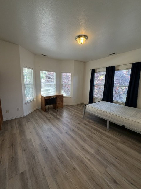 Spacious room with wood-finish flooring, a bay window feature, and multiple windows providing natural light