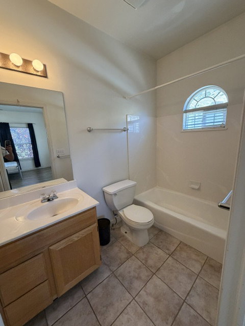Bathroom featuring a wood-finish vanity with an integrated sink, a full-width mirror, tile flooring, a tub/shower combination, and an arched window with blinds