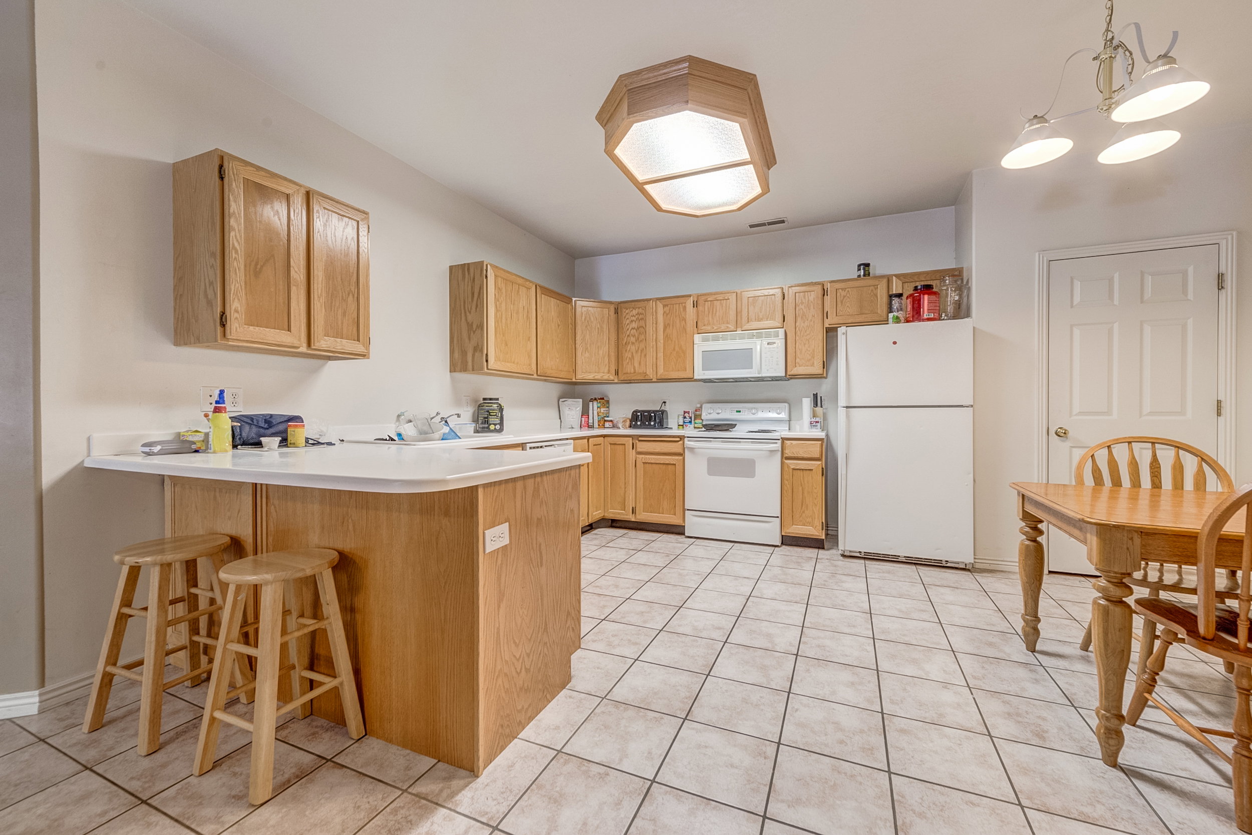 Kitchen featuring tile flooring, oak cabinetry, white countertops, and white appliances