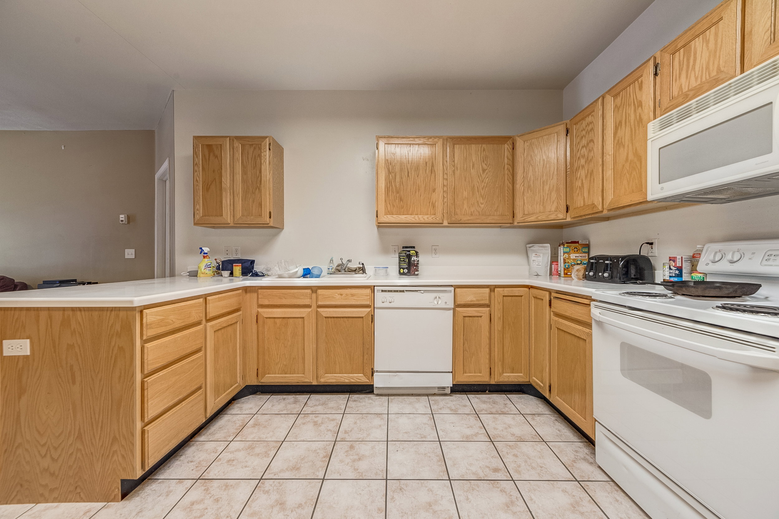 Kitchen featuring wood-finish cabinetry, white countertops, tile flooring, and white appliances including a dishwasher, range, and built-in microwave