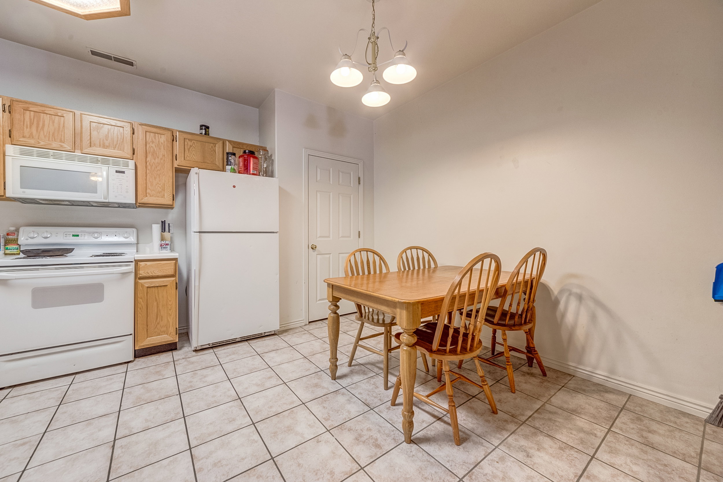 Kitchen area featuring tile flooring, wood cabinetry, white appliances, and a built-in ceiling light fixture