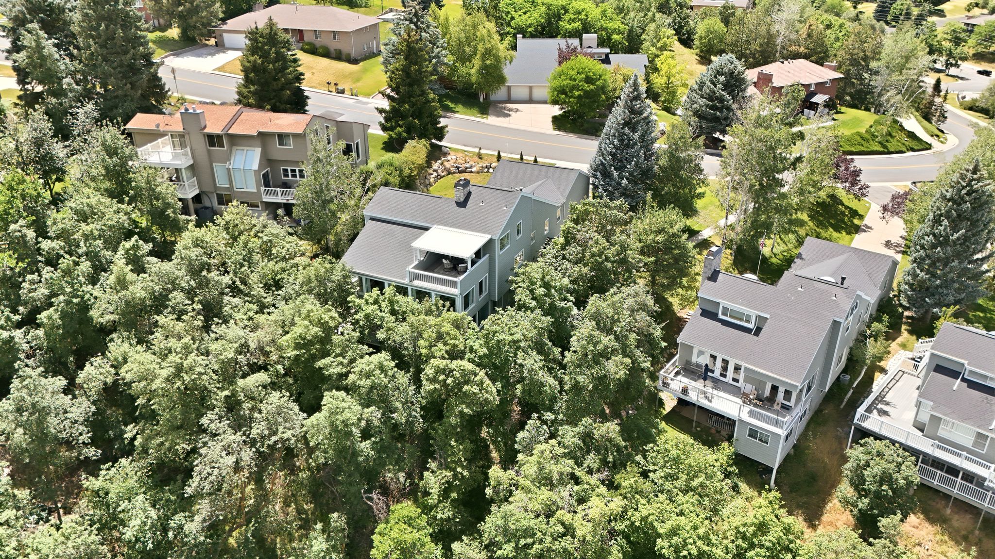 Property featuring multiple balconies, a dark shingle roof, and light-colored siding with heavily wooded privacy