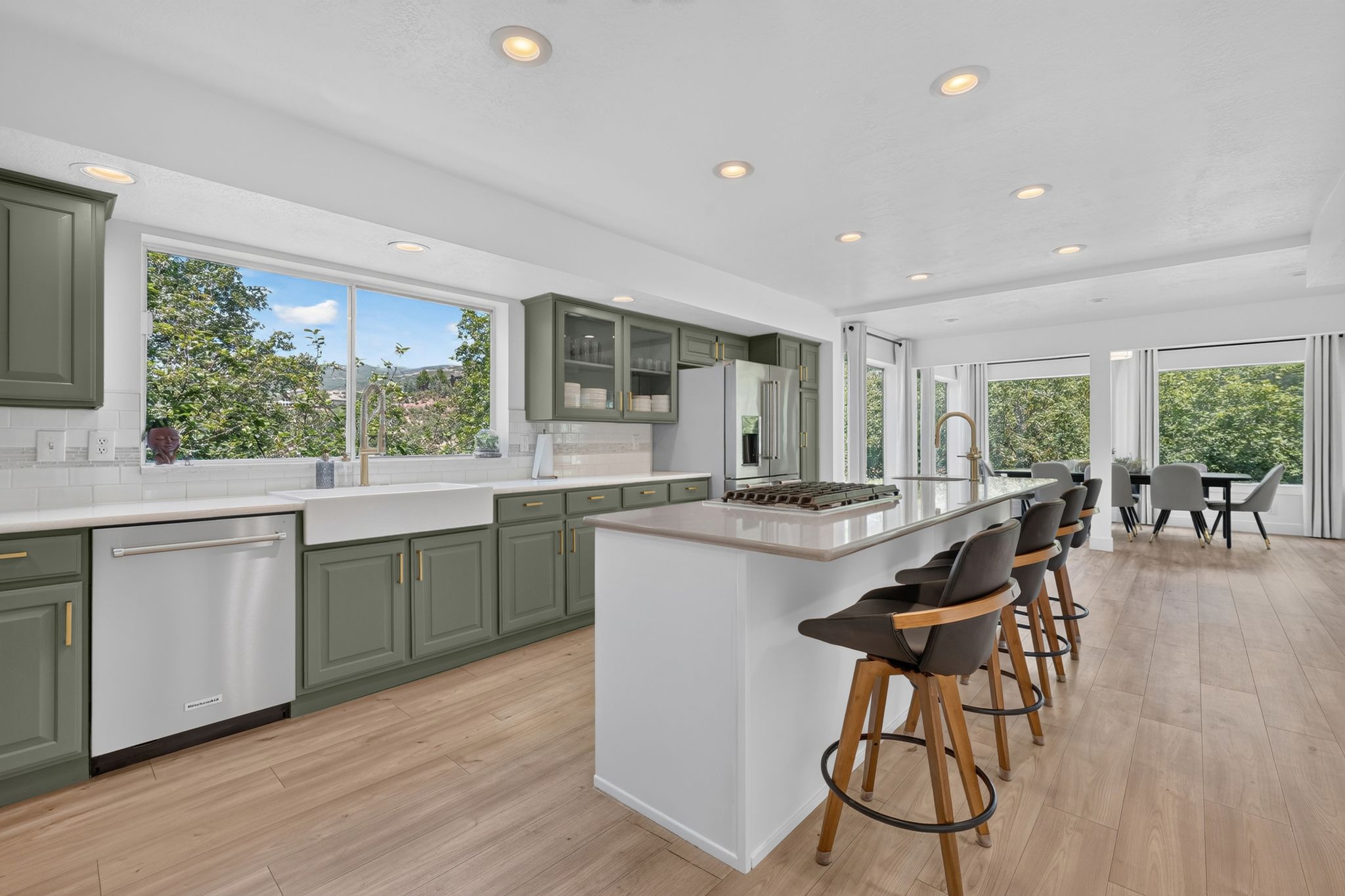 Gourmet kitchen featuring sage-toned cabinetry, a large center island with counter seating, stainless steel appliances, a farmhouse sink, and wood-finish flooring