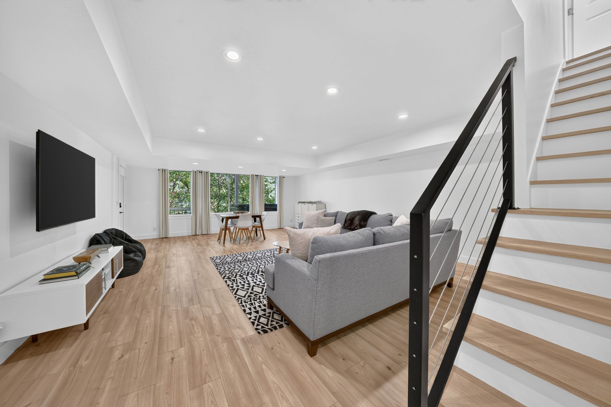 Open-concept living space featuring wood-finish flooring, recessed lighting, and a modern staircase with cable railing