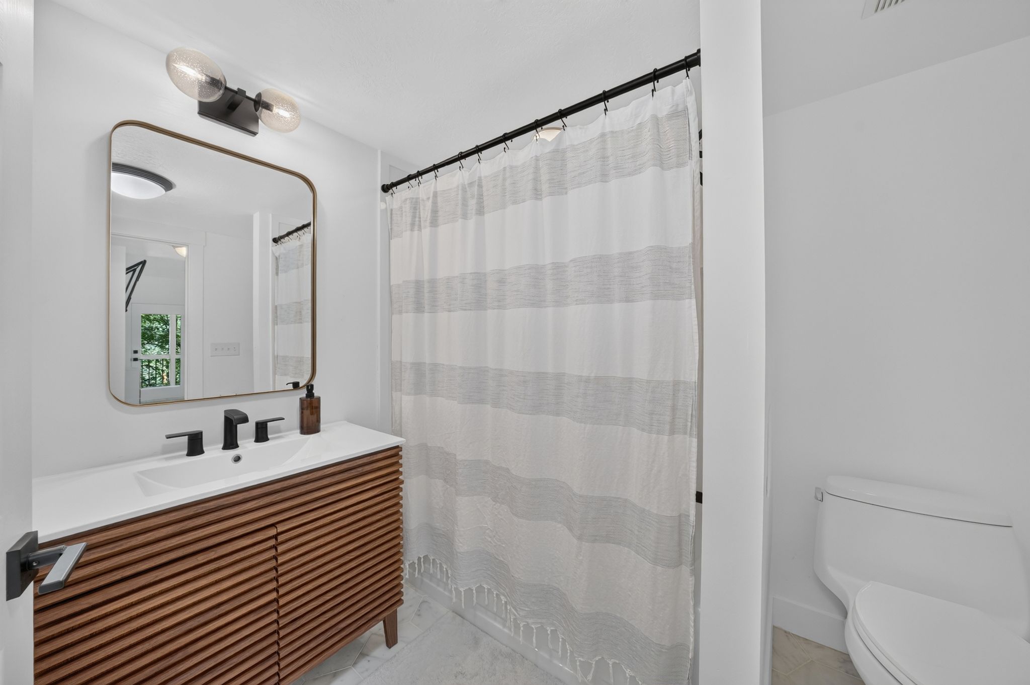 Contemporary bathroom featuring a slatted wood-finish vanity, integrated sink, and matte black fixtures
