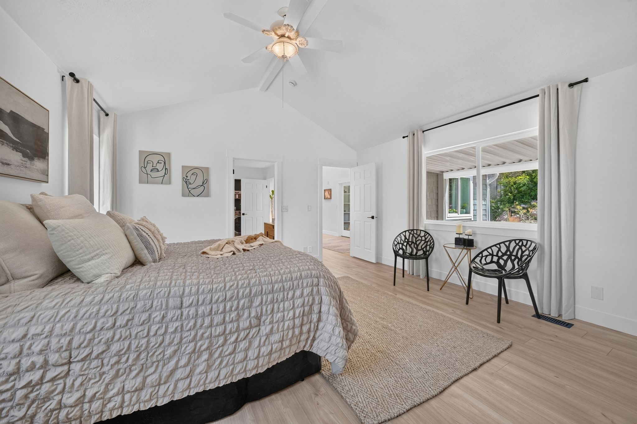 Spacious bedroom featuring vaulted ceilings, a ceiling fan with integrated lighting, wood-finish flooring, and a large window with white trim
