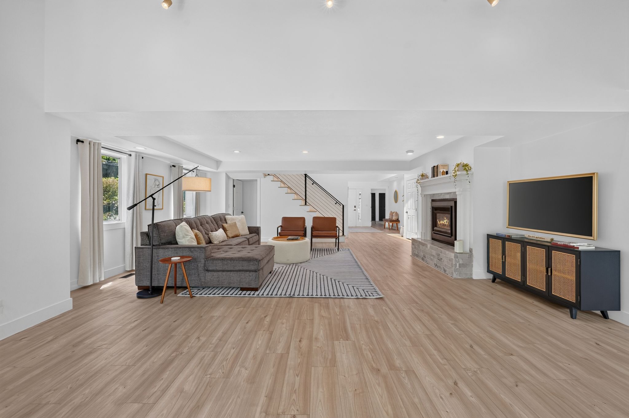 Spacious living area featuring wood-finish flooring, a stone-faced fireplace with a white mantel, and ample natural light from multiple windows