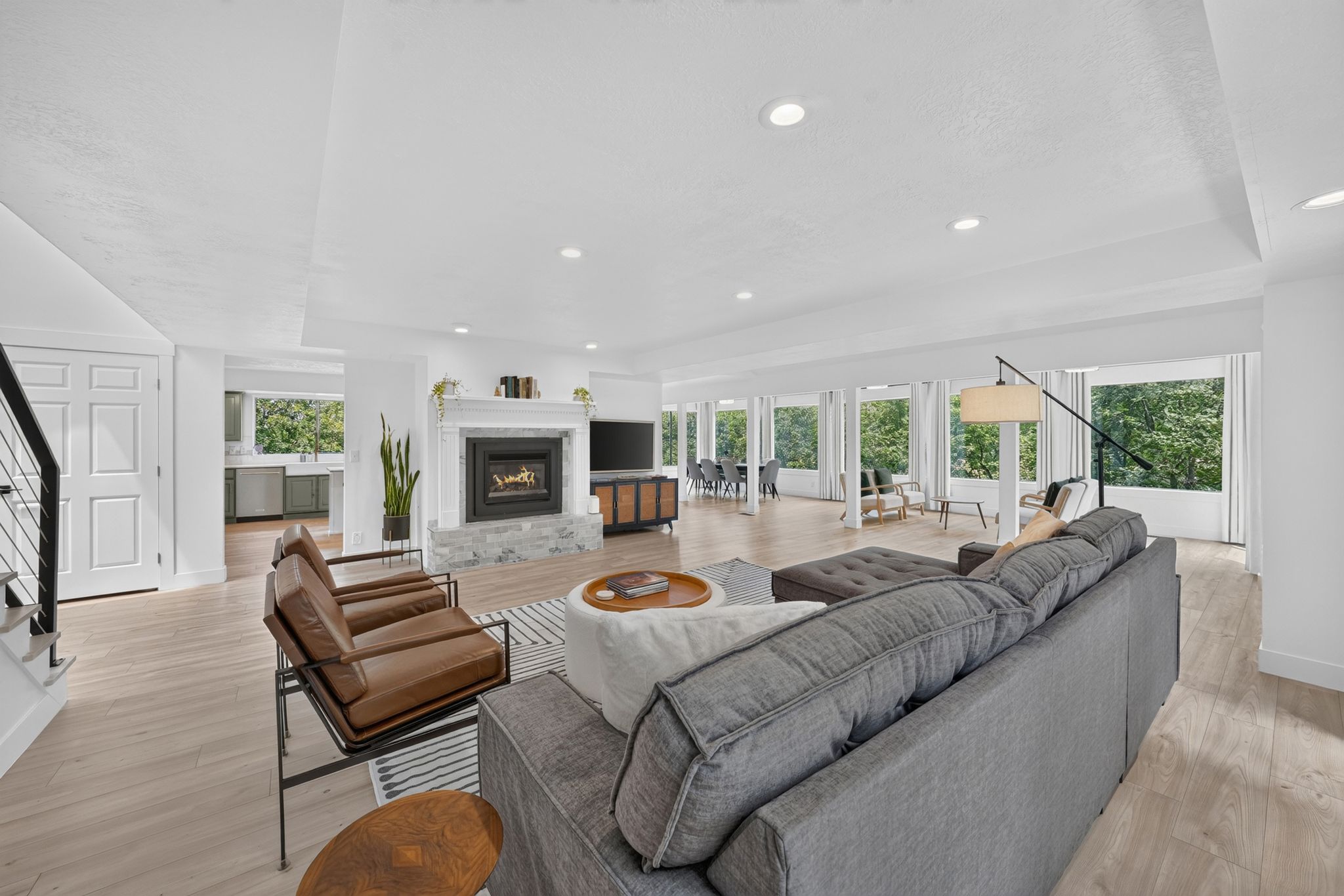 Spacious living area featuring light wood-finish flooring, recessed lighting, and a modern fireplace with a white mantel and stone surround