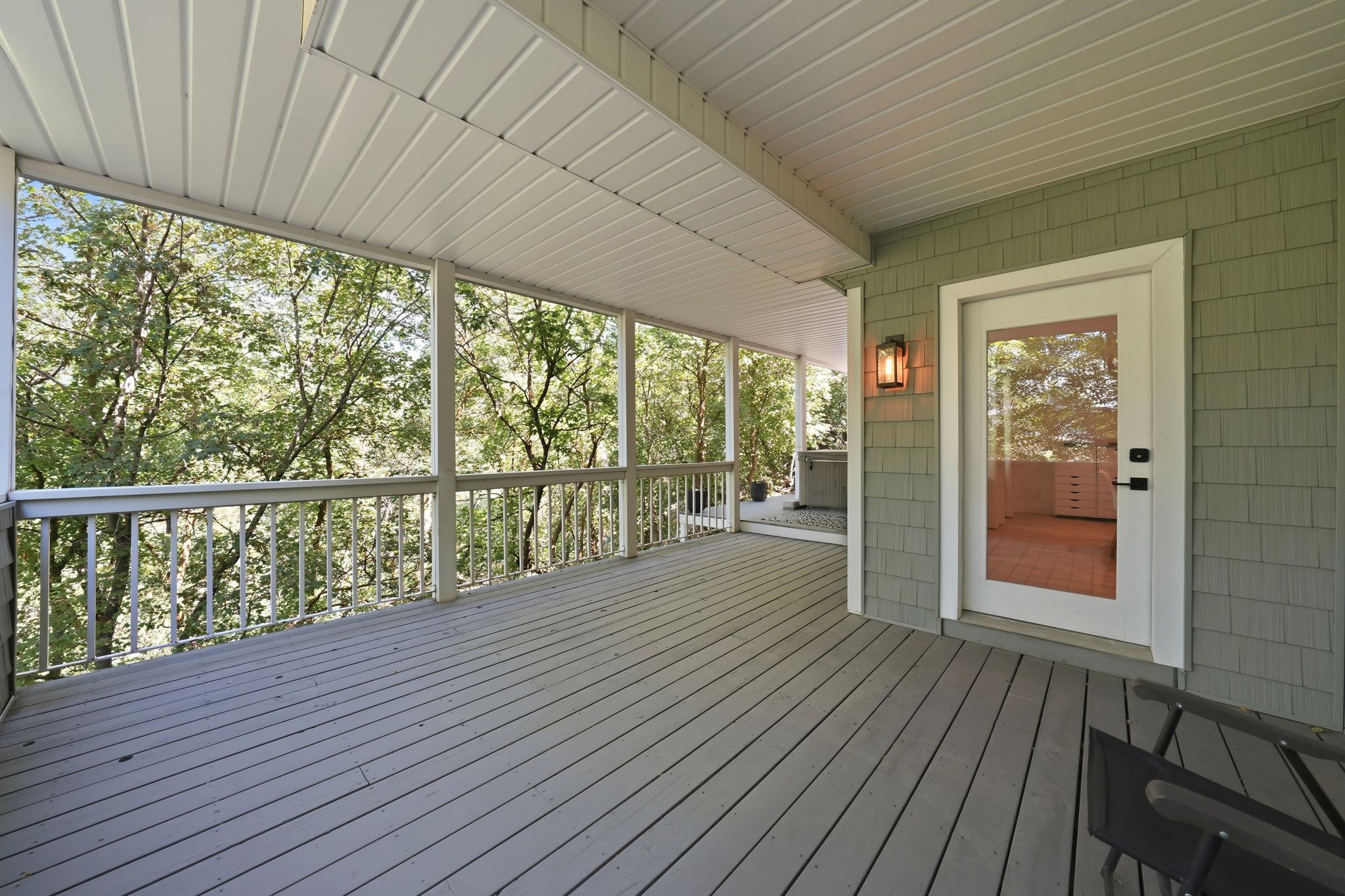 Expansive covered deck featuring wood-finish flooring, white spindle railings, and a full-light glass door