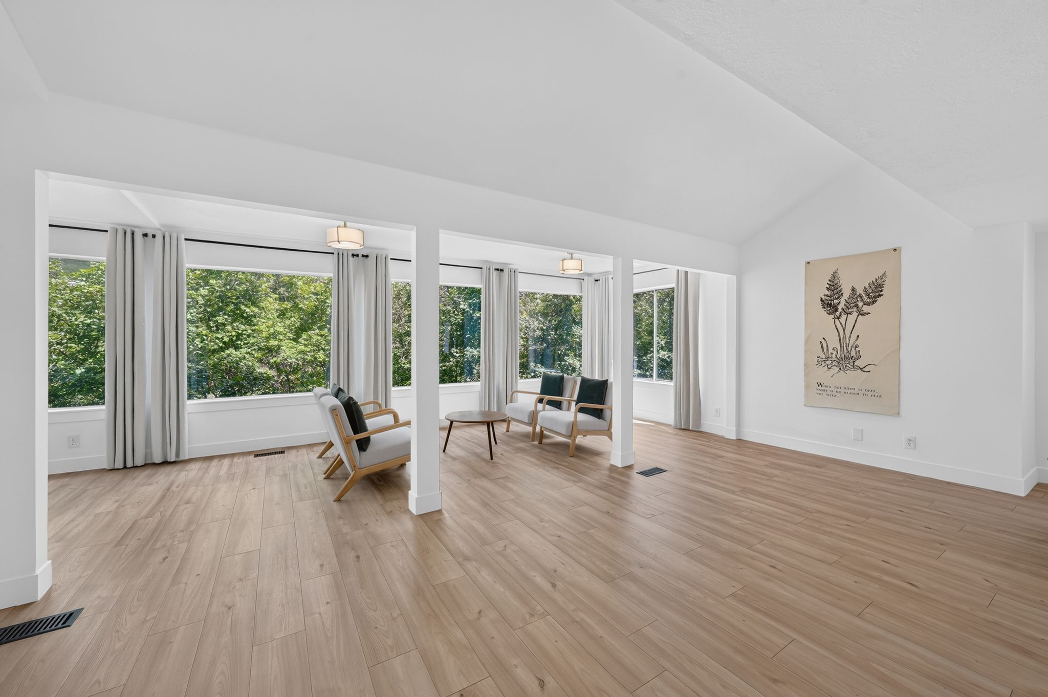 Expansive room featuring wood-finish flooring, vaulted ceilings, and a wall of windows