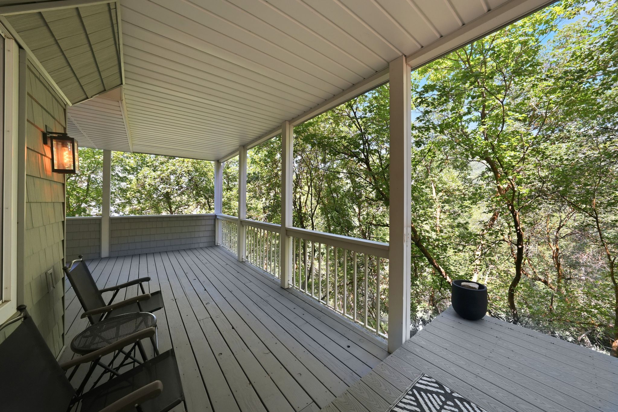 Expansive covered porch featuring wood flooring, white railings, and a shingled exterior wall with an exterior light fixture