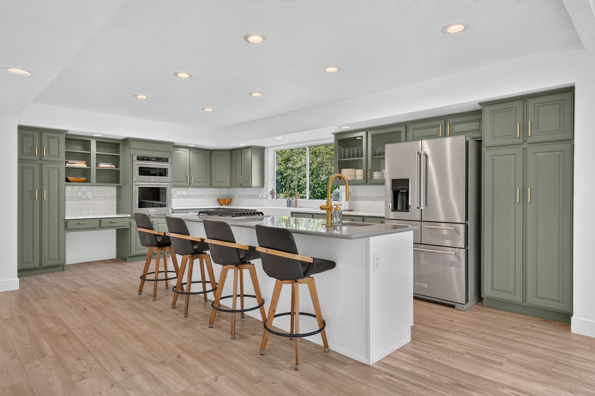Spacious kitchen featuring sage green cabinetry, stainless steel appliances, a large center island with counter seating, and wood-finish flooring