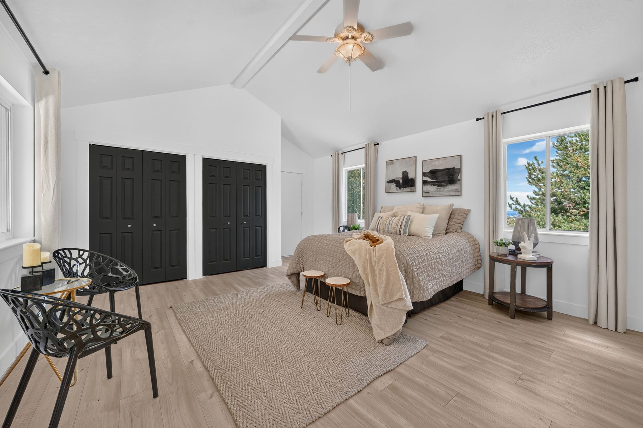 Spacious room featuring vaulted ceilings, light wood-finish flooring, two large windows, and a ceiling fan with integrated lighting