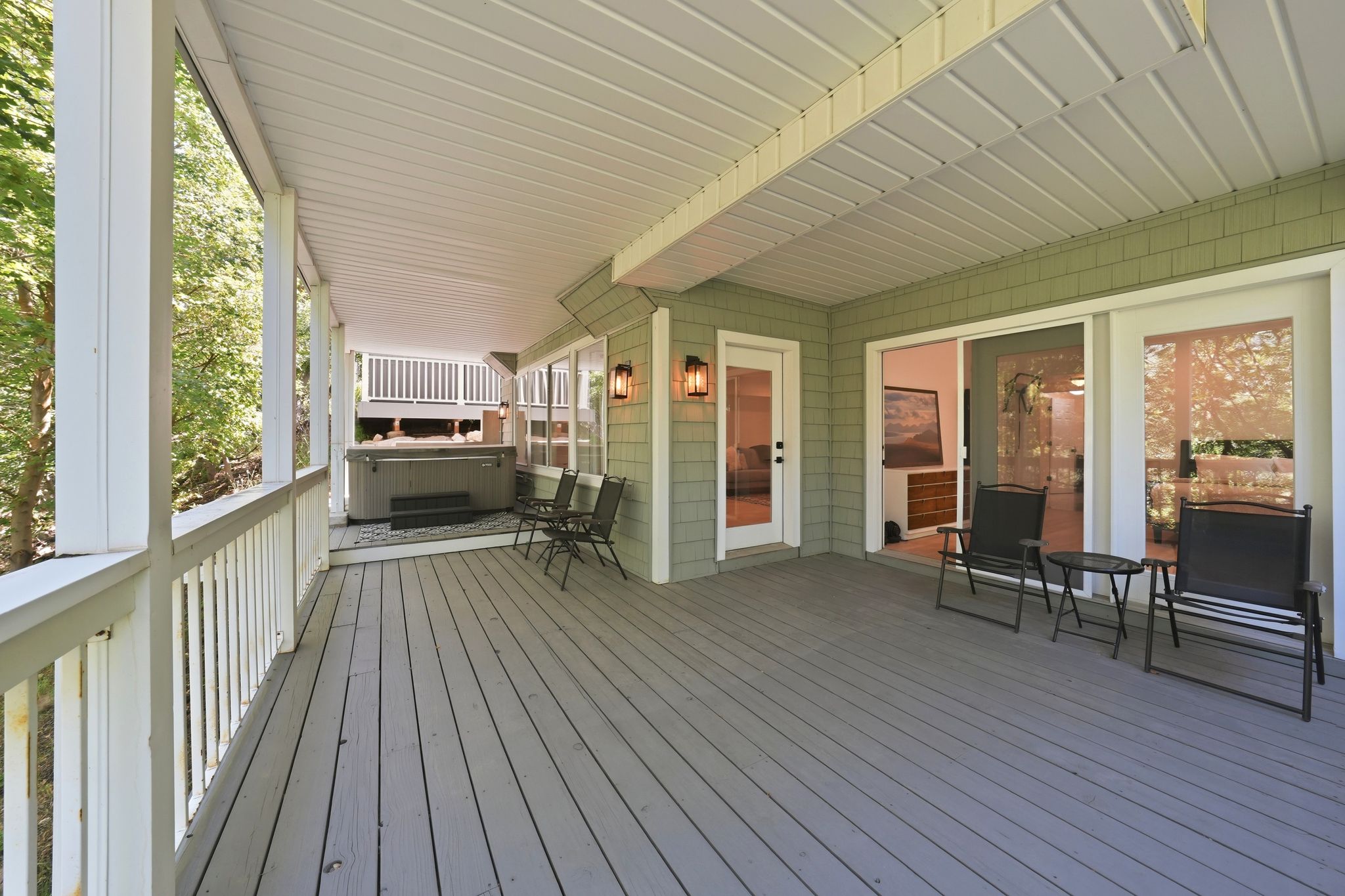 Expansive covered deck featuring wood-finish flooring, a built-in hot tub, and multiple exterior access points