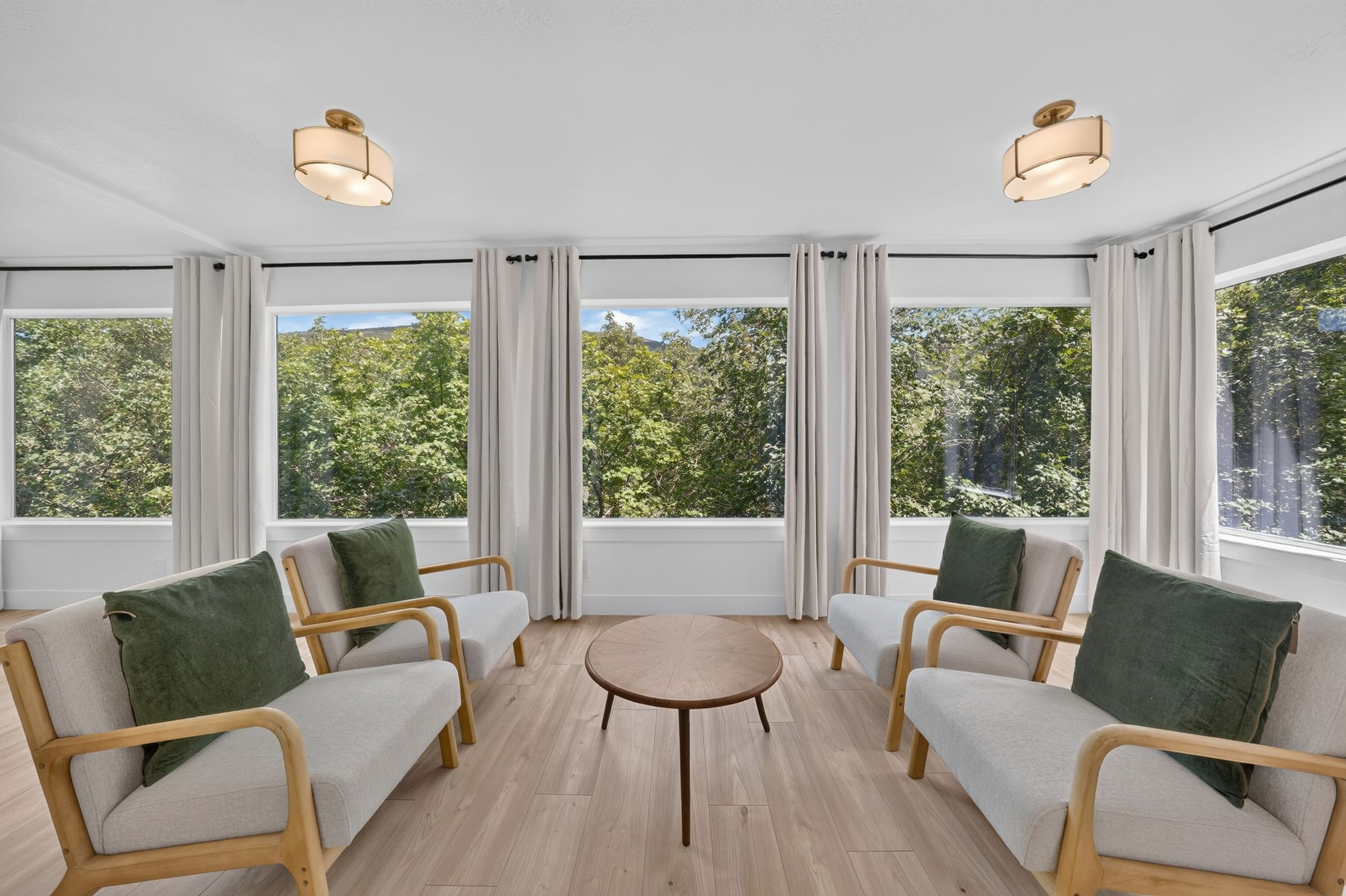 Room featuring extensive window walls, wood-finish flooring, two flush mount ceiling lights, and light-colored curtains