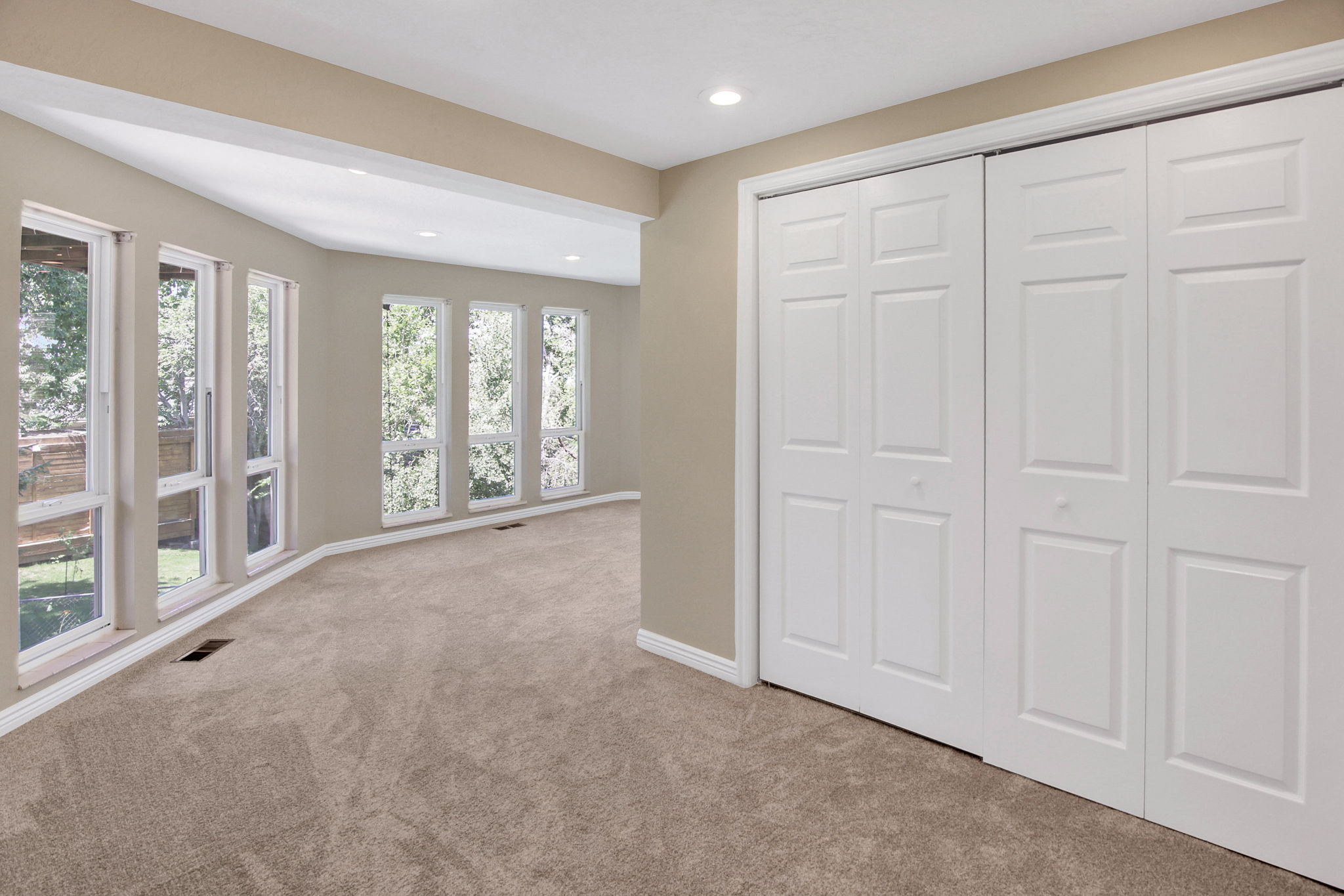 Lower level primary suite. Carpeted room featuring multiple tall windows overlooking exterior greenery, closet and sitting area