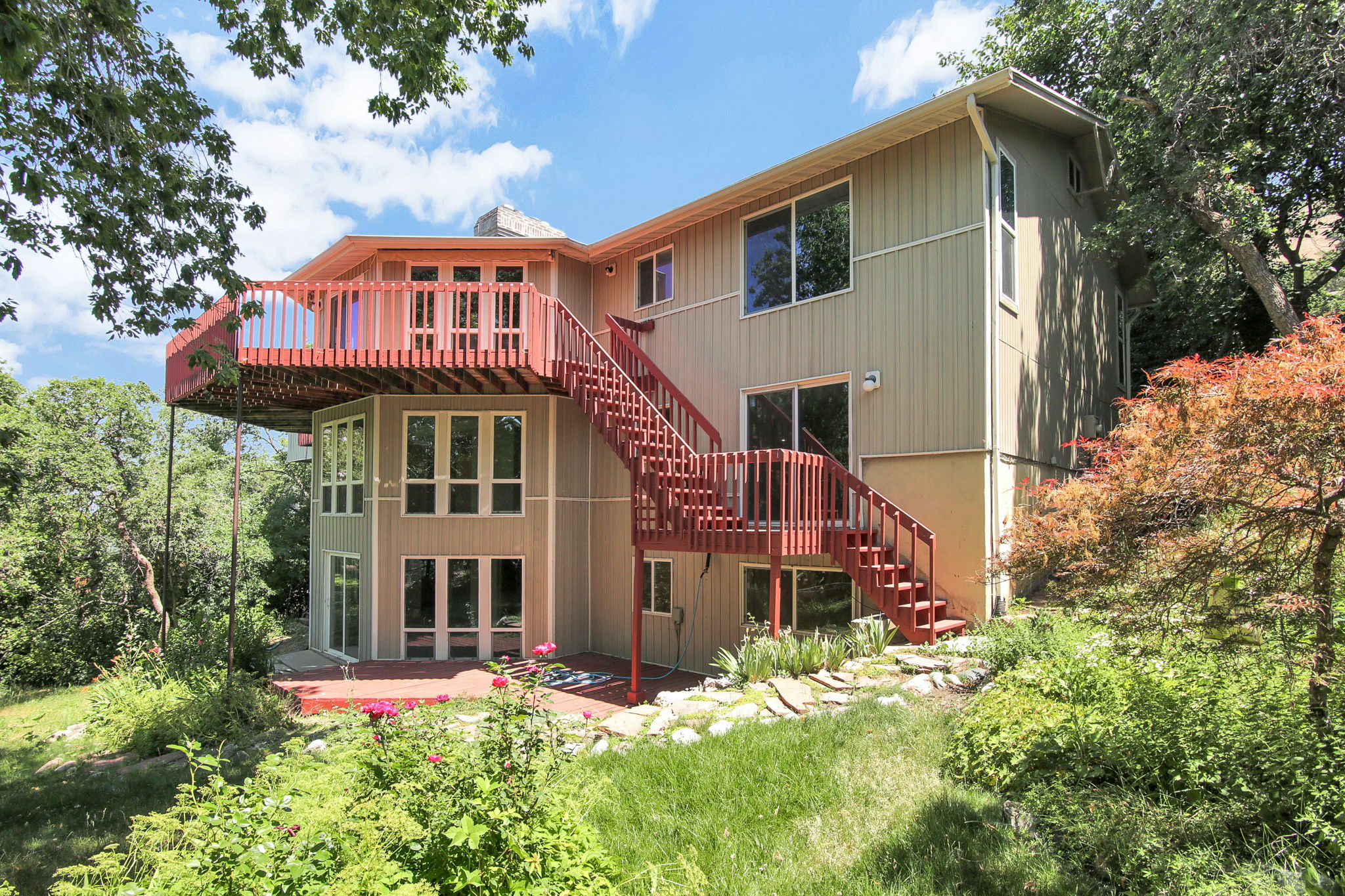 Multi-level exterior featuring newer siding, a large upper-level deck, and a lower-level patio