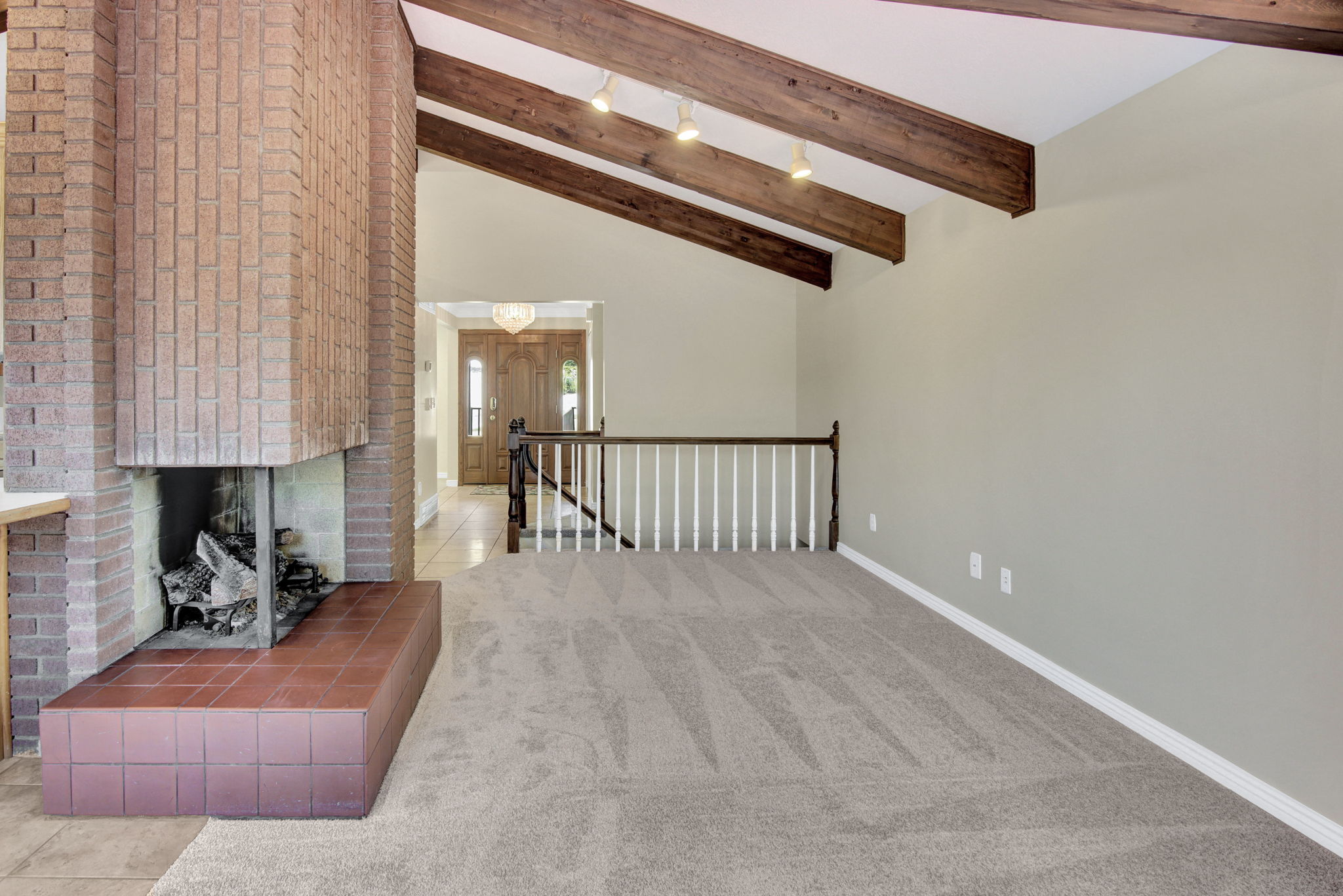 Living area featuring a floor-to-ceiling brick fireplace with a tile hearth, vaulted ceilings with exposed wood beams, and neutral-toned carpeting
