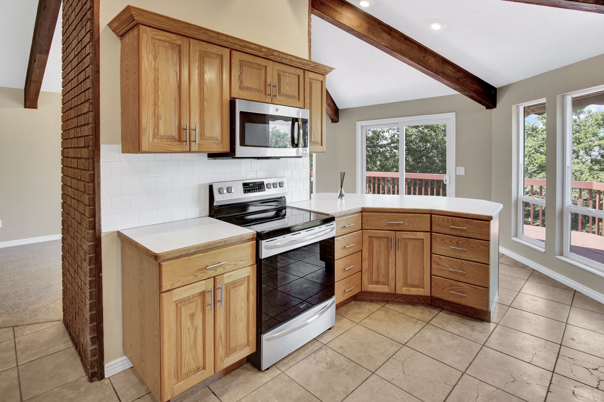 Well-appointed kitchen featuring wood cabinetry, new cab. handles, stainless steel appliances, and a white tile backsplash. open to family room & deck