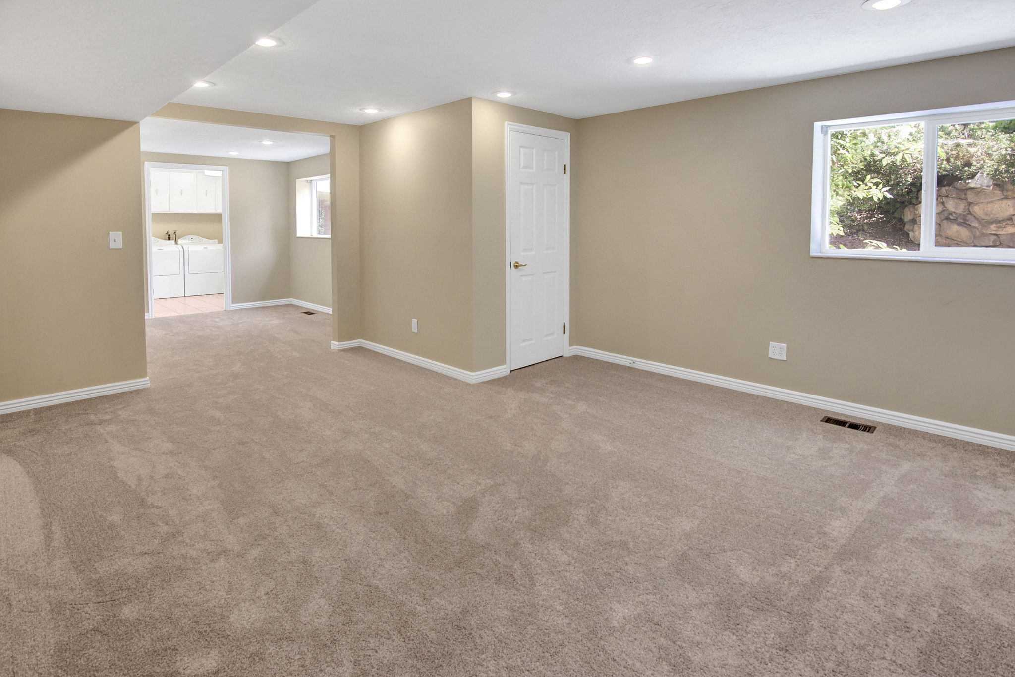 Spacious room with large windows. View to potential kitchen space and large finished laundry