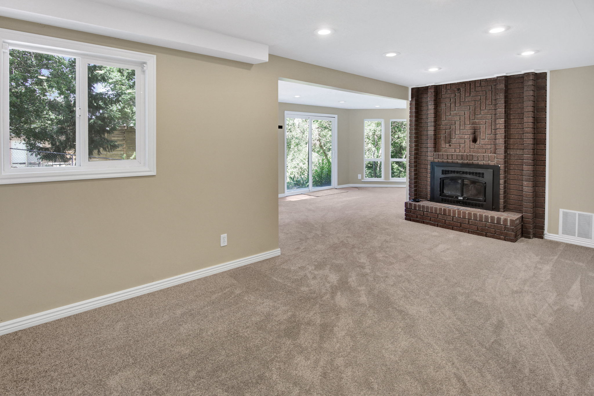 Spacious living area featuring a prominent brick fireplace with hearth, recessed lighting, and neutral carpeting. Slider to outside patio/deck