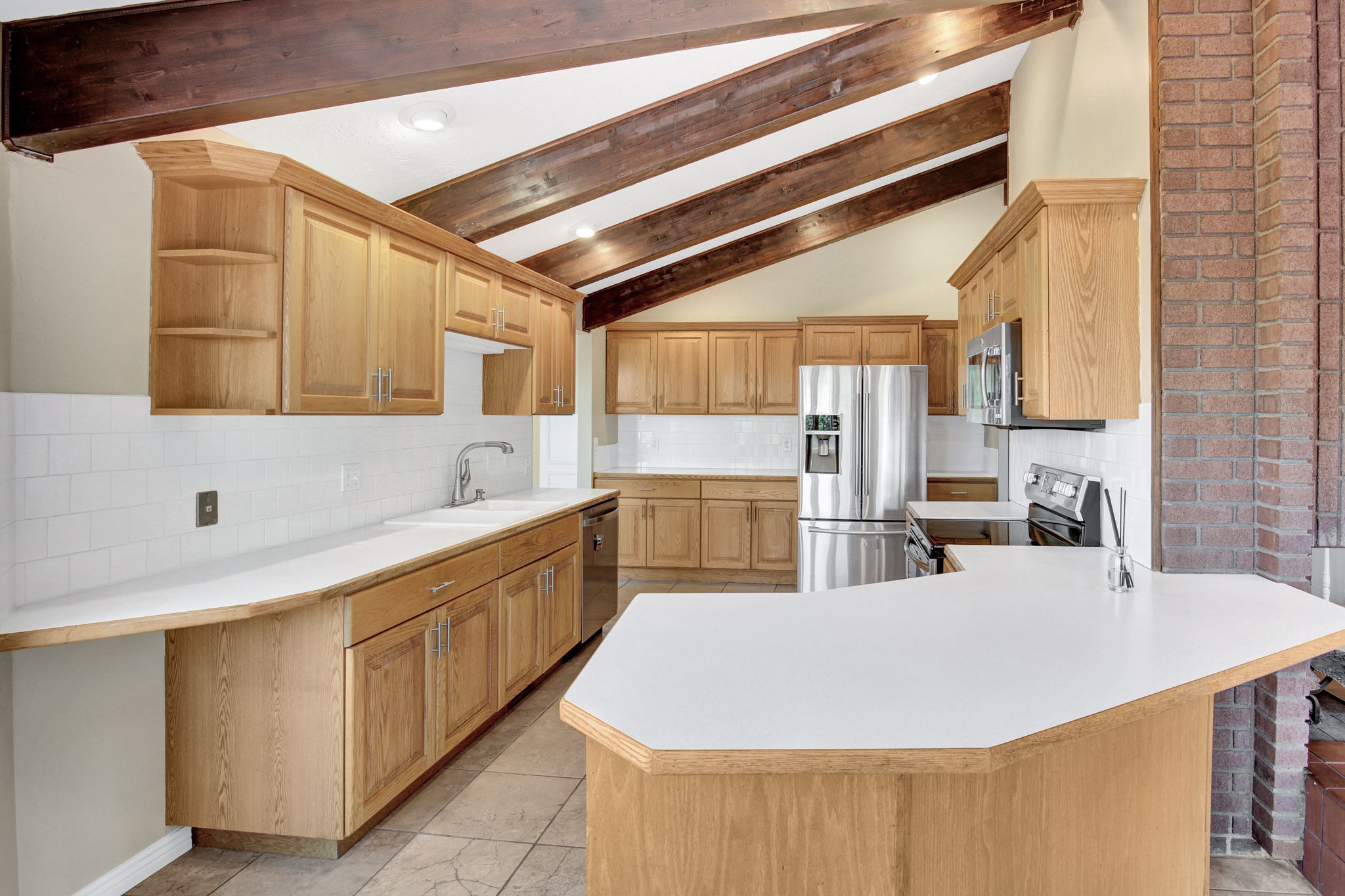 Kitchen featuring wood-finish cabinetry, light countertops, and vaulted ceilings with exposed wood beams