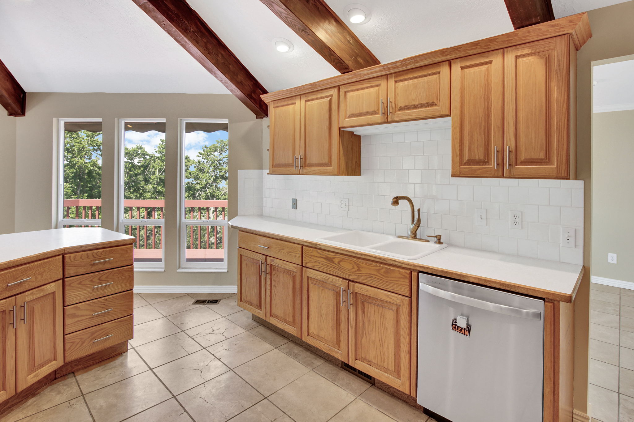 Kitchen featuring natural wood cabinetry with brushed nickel hardware, a white tile backsplash, and light-toned countertops. Newer appliances
