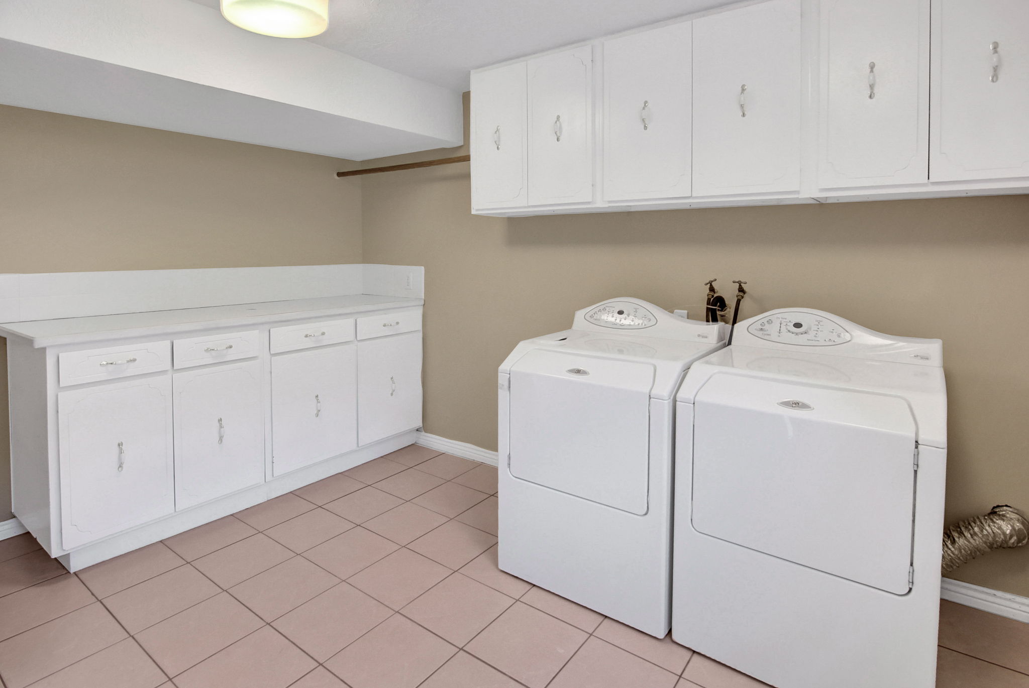 Laundry room featuring tile flooring, extensive white cabinetry, a built-in countertop, and washer/dryer