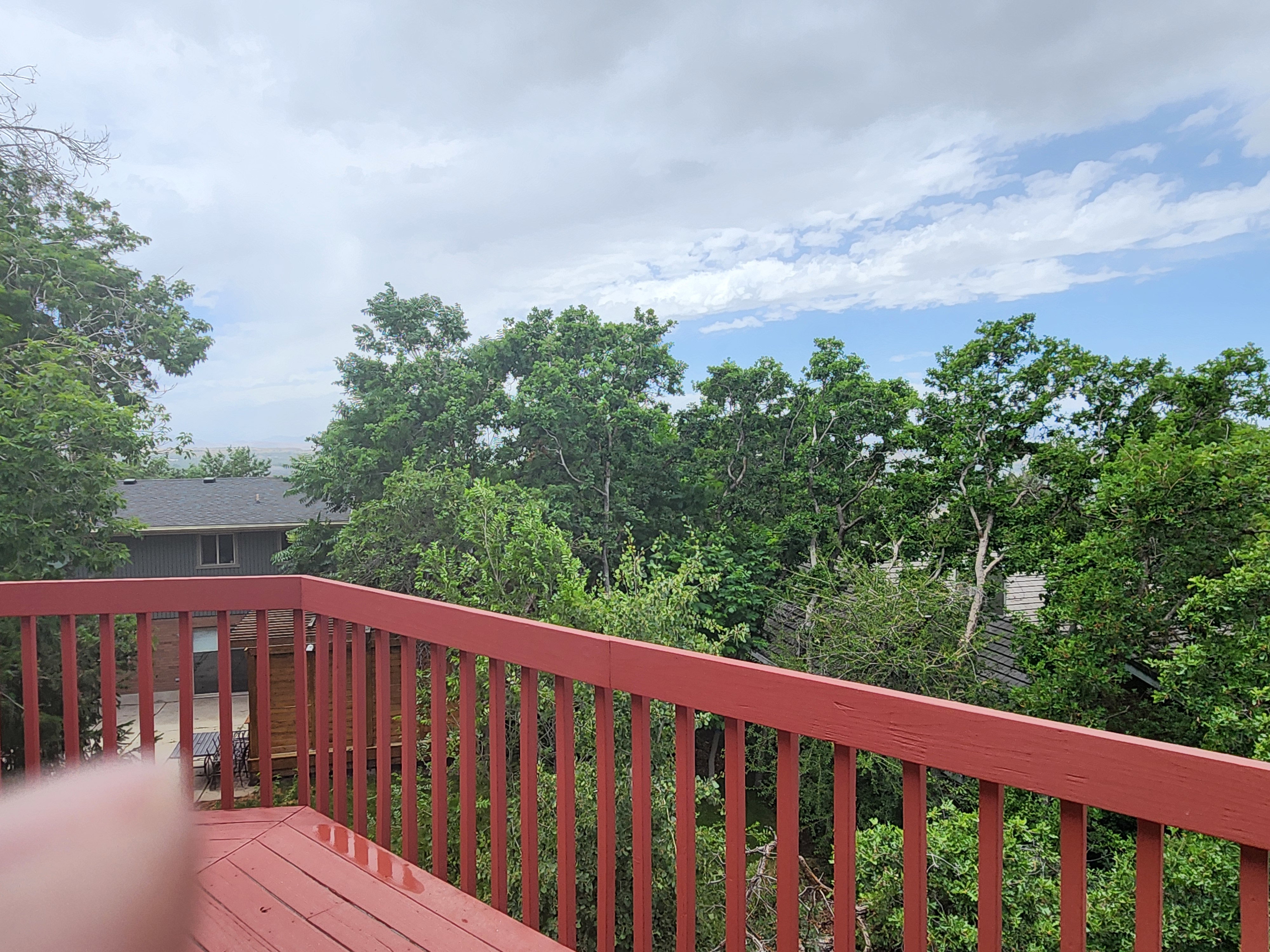 Deck featuring red-painted wood construction and a surrounding canopy of mature trees