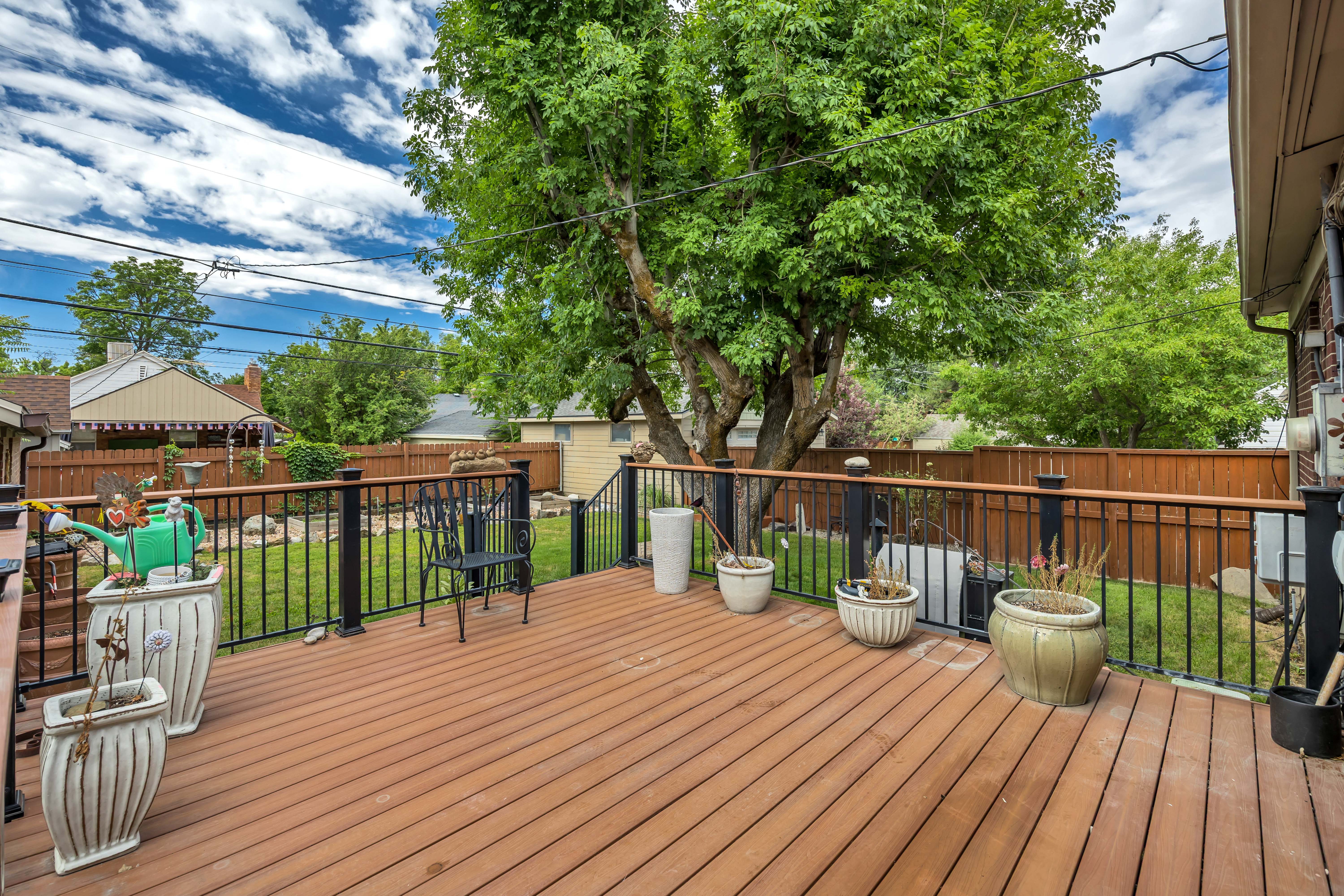 Spacious rear deck featuring wood-finish decking, black metal railings with wood-finish top rails, and a large mature tree providing natural coverage