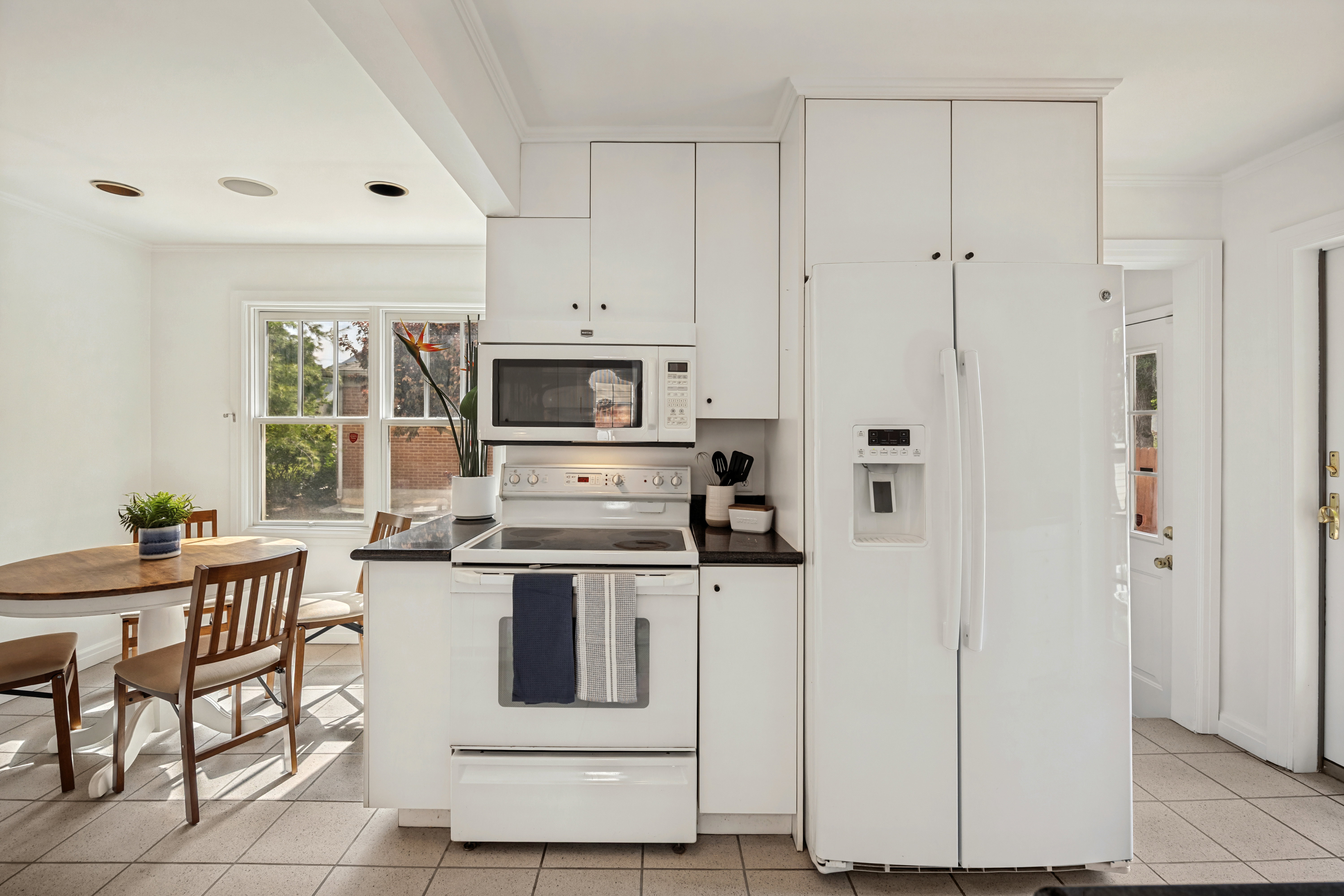 Bright kitchen featuring white cabinetry, a white appliance suite, dark countertops, and tile flooring