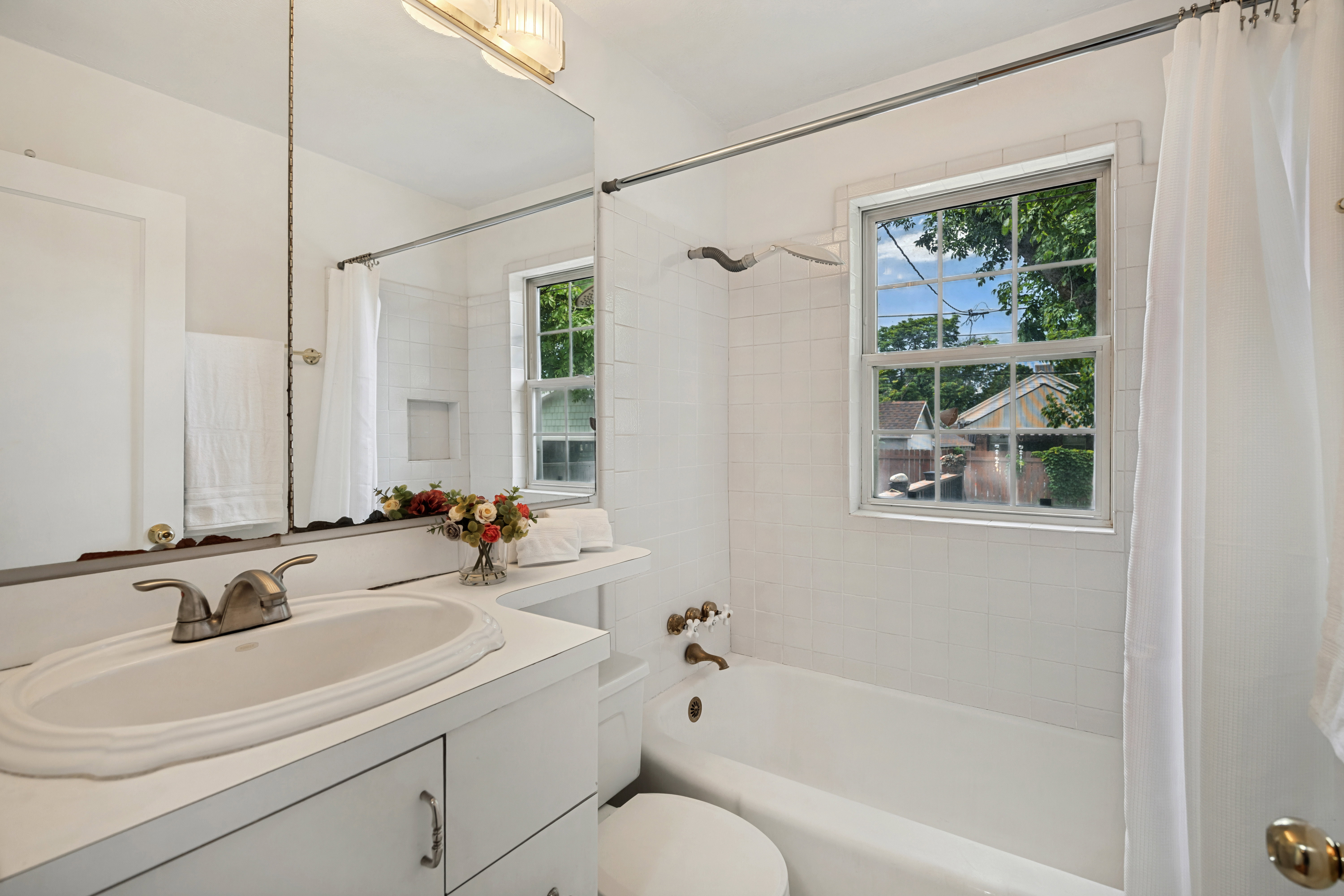 Bathroom featuring a window above the tub, white subway tile surround, white vanity with integrated sink, and an expansive mirror