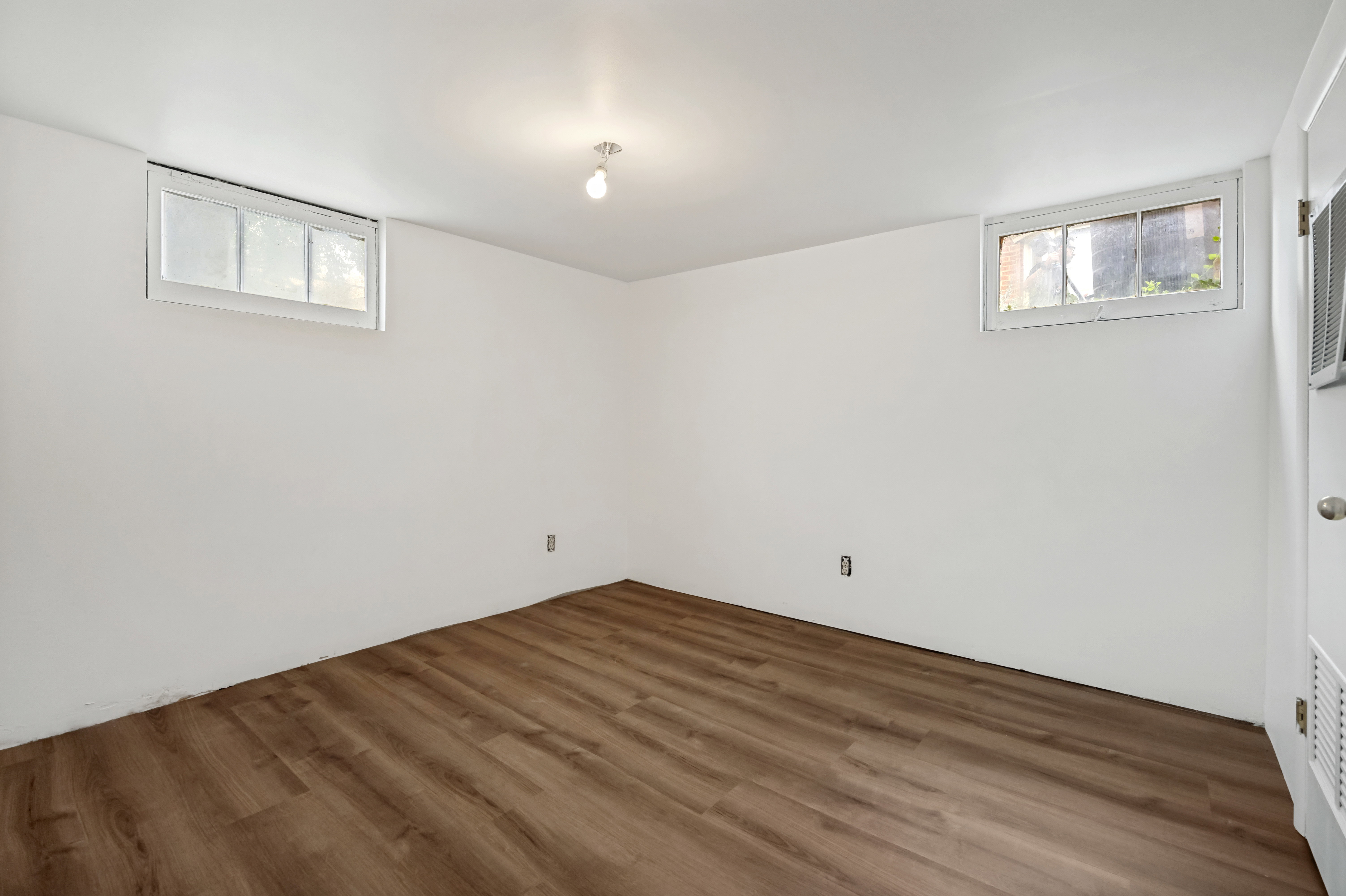 Room featuring wood-finish flooring, white walls, two windows, and a ceiling-mounted light fixture